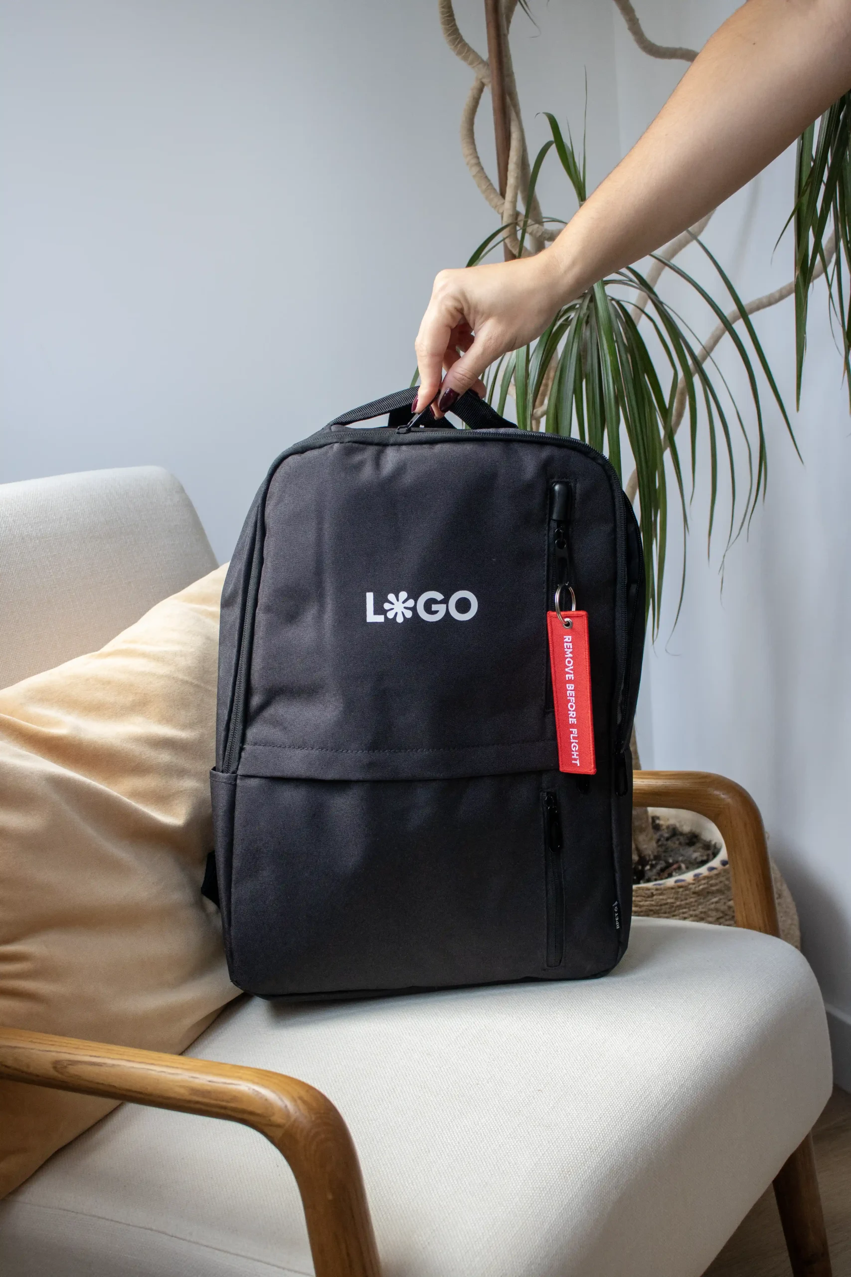 Mano agarrando una mochila negra con un llavero rojo de tela colgado en la cremallera