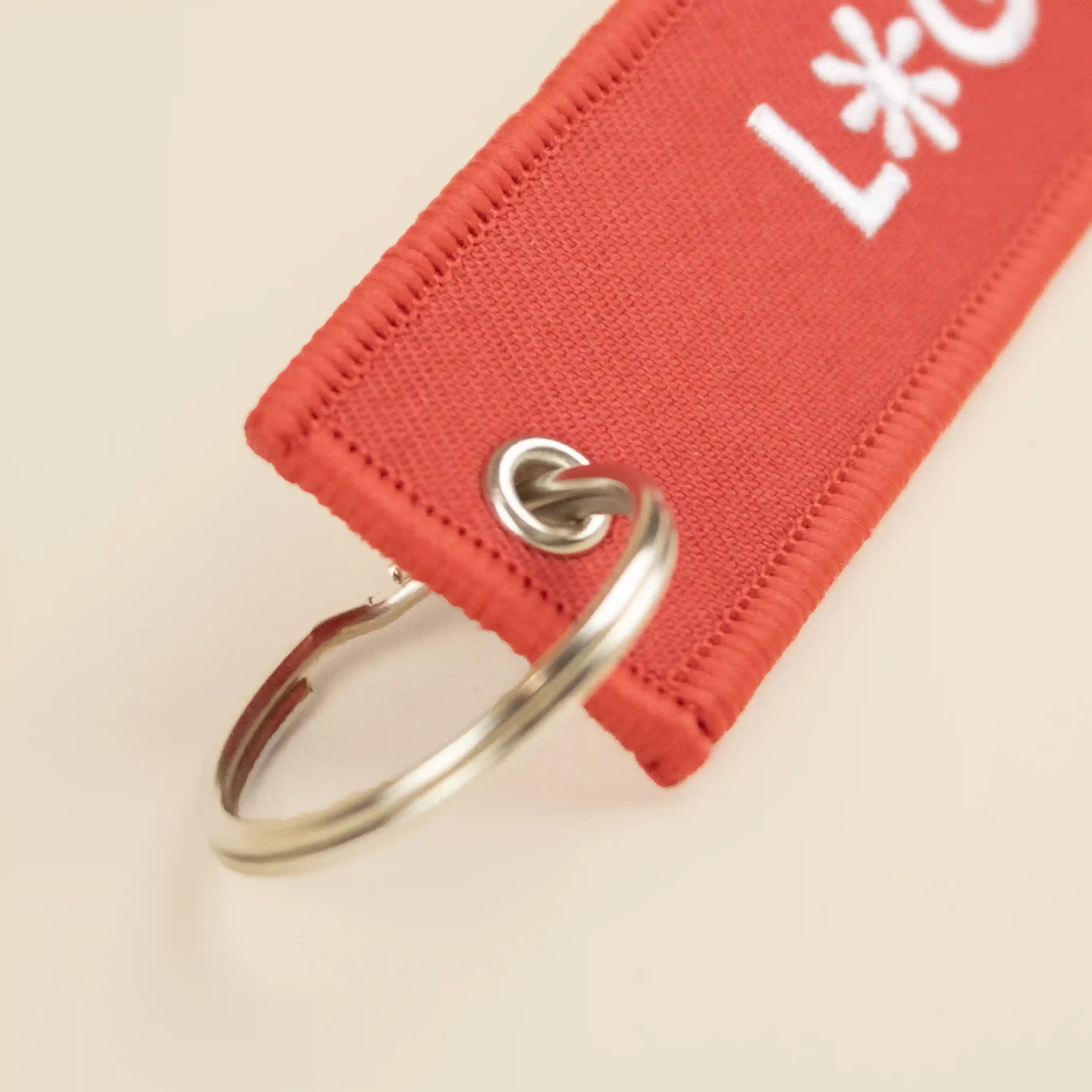 Anilla metálica de un llavero de tela rojo bordado con logo blanco
