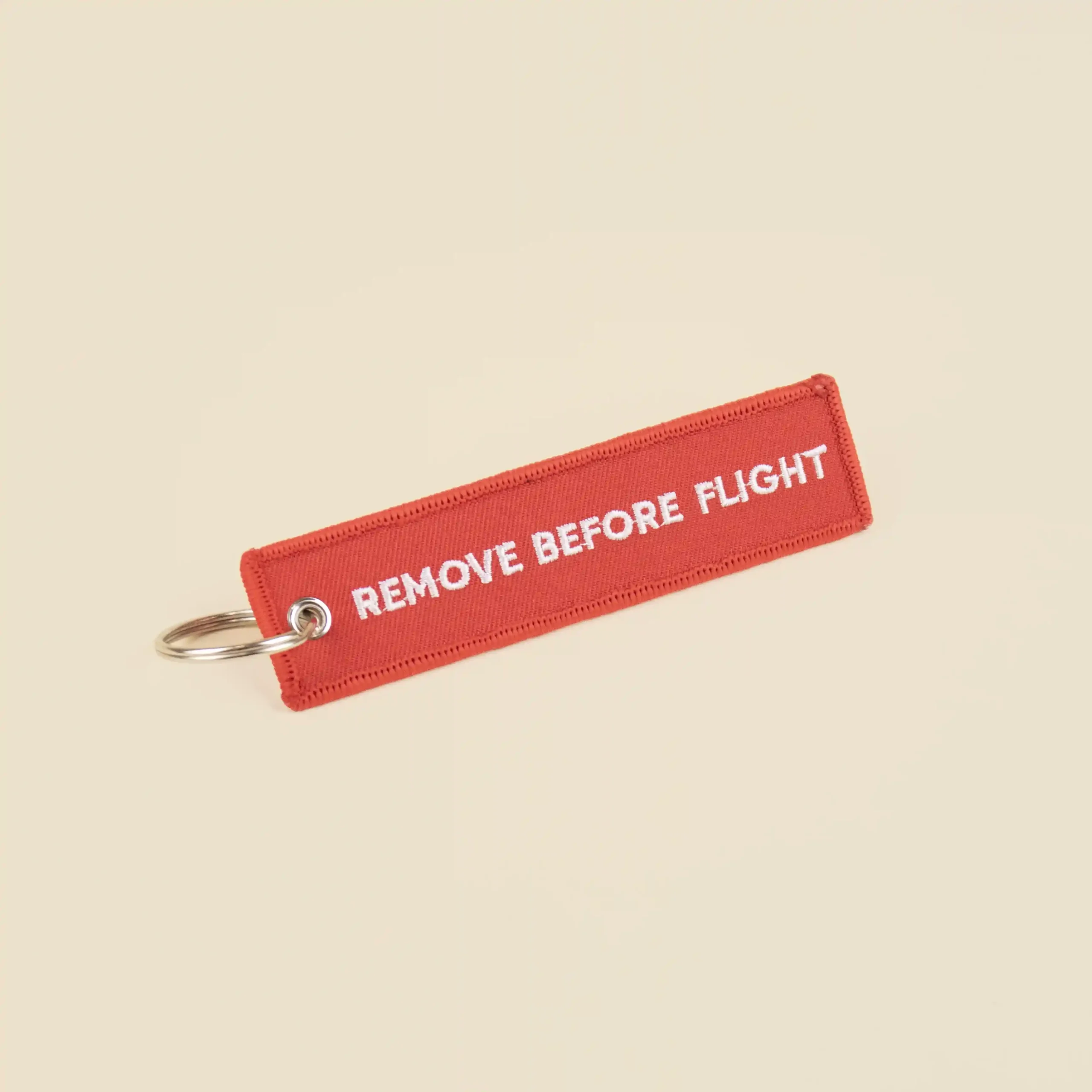 Llavero de tela rojo personalizado bordado con hilo blanco sobre fondo beige