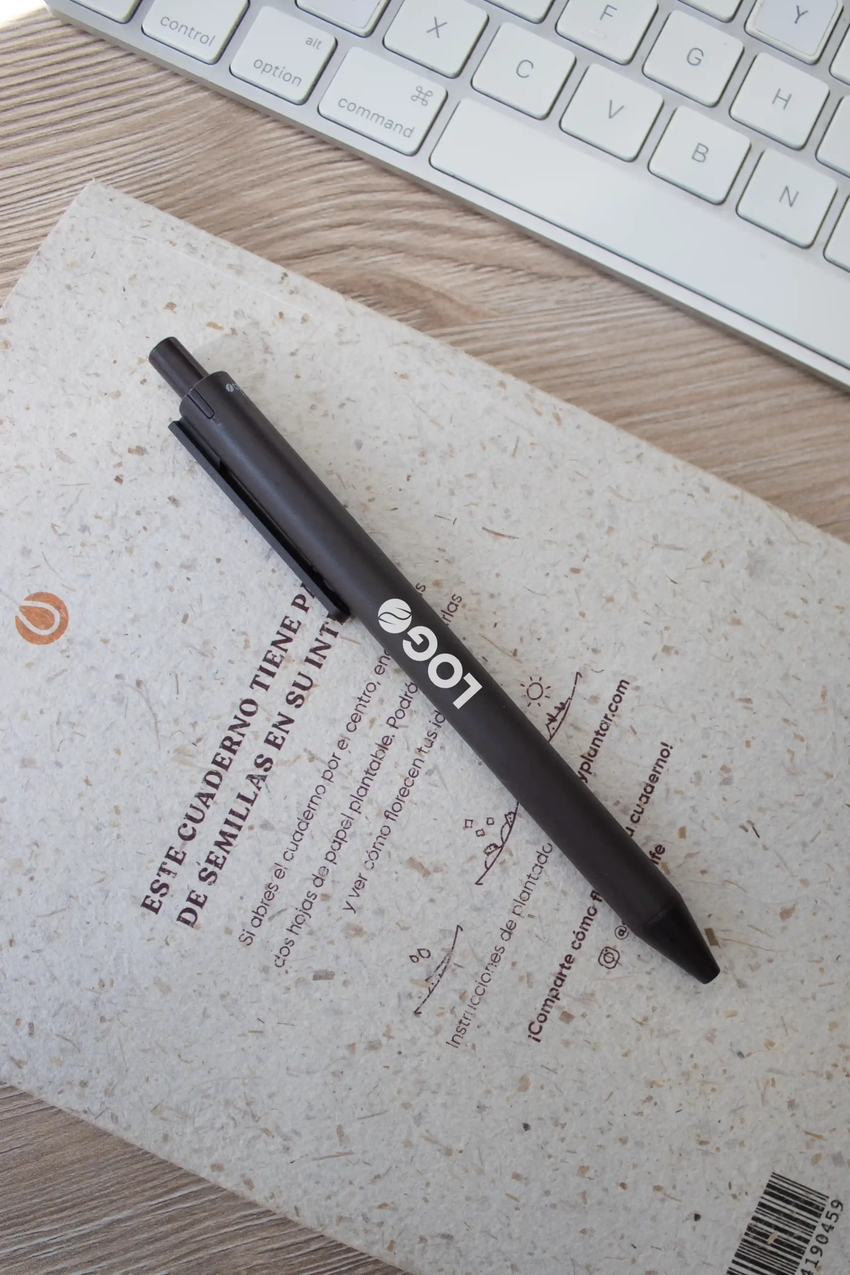 Bolígrafo marrón con la palabra logo en blanco impreso junto a un cuaderno y un teclado de ordenador