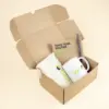 Caja de cartón abierta con un neceser beige, una taza blanca, un cuaderno kraft y un bolígrafo marrón personalizados con logo
