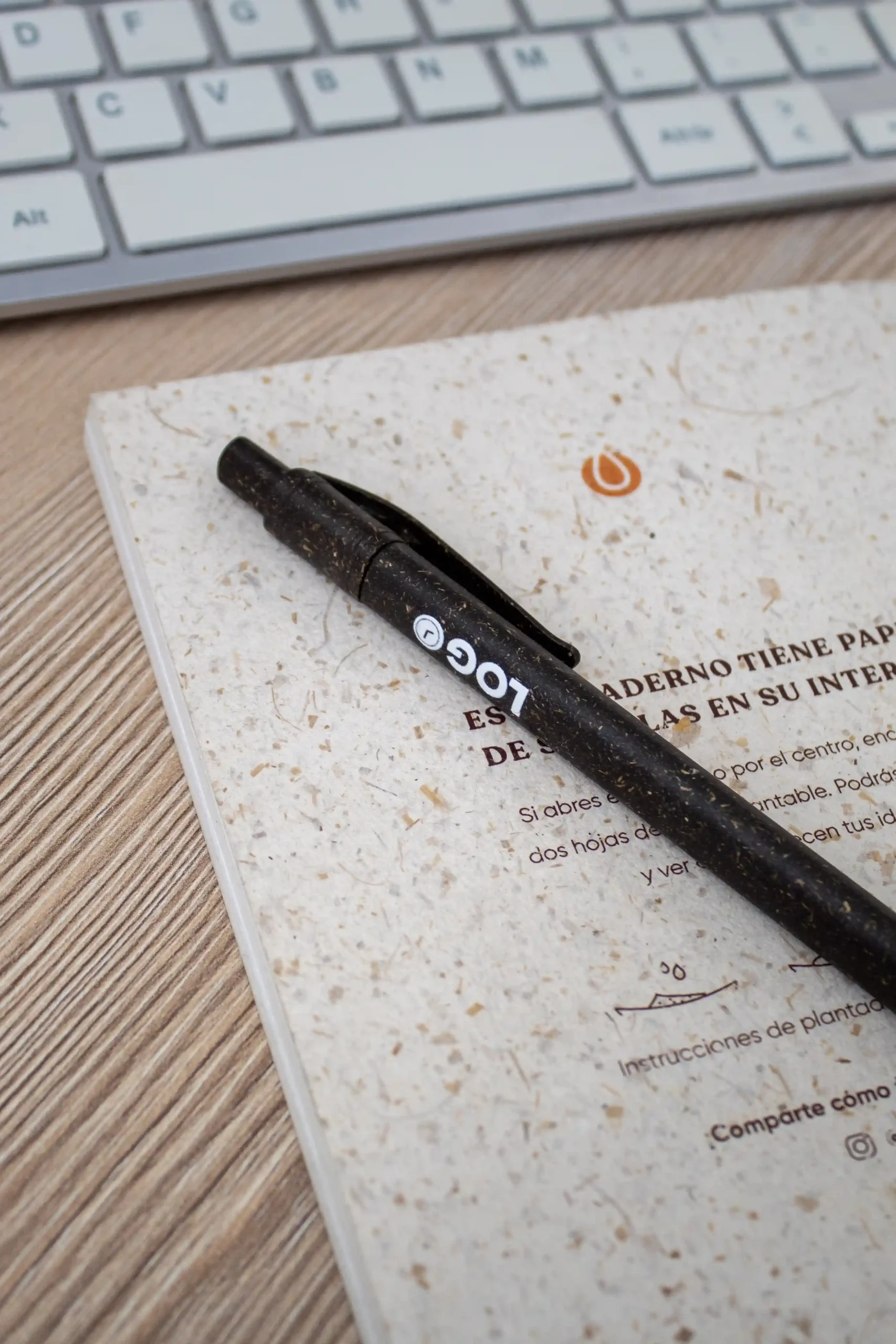 Bolígrafo marrón con la palabra logo en blanco impreso junto a un cuaderno y un teclado de ordenador