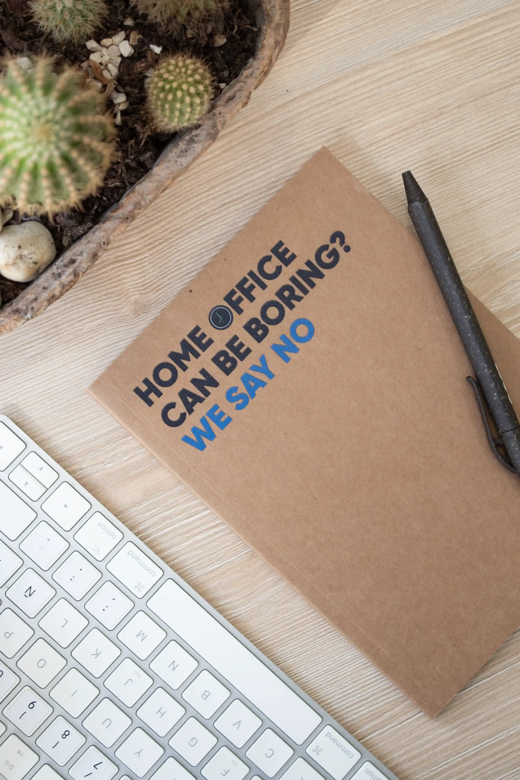 Cuaderno kraft personalizado sobre una mesa de madera junto a una planta, un bolígrafo marrón y un teclado de ordenador