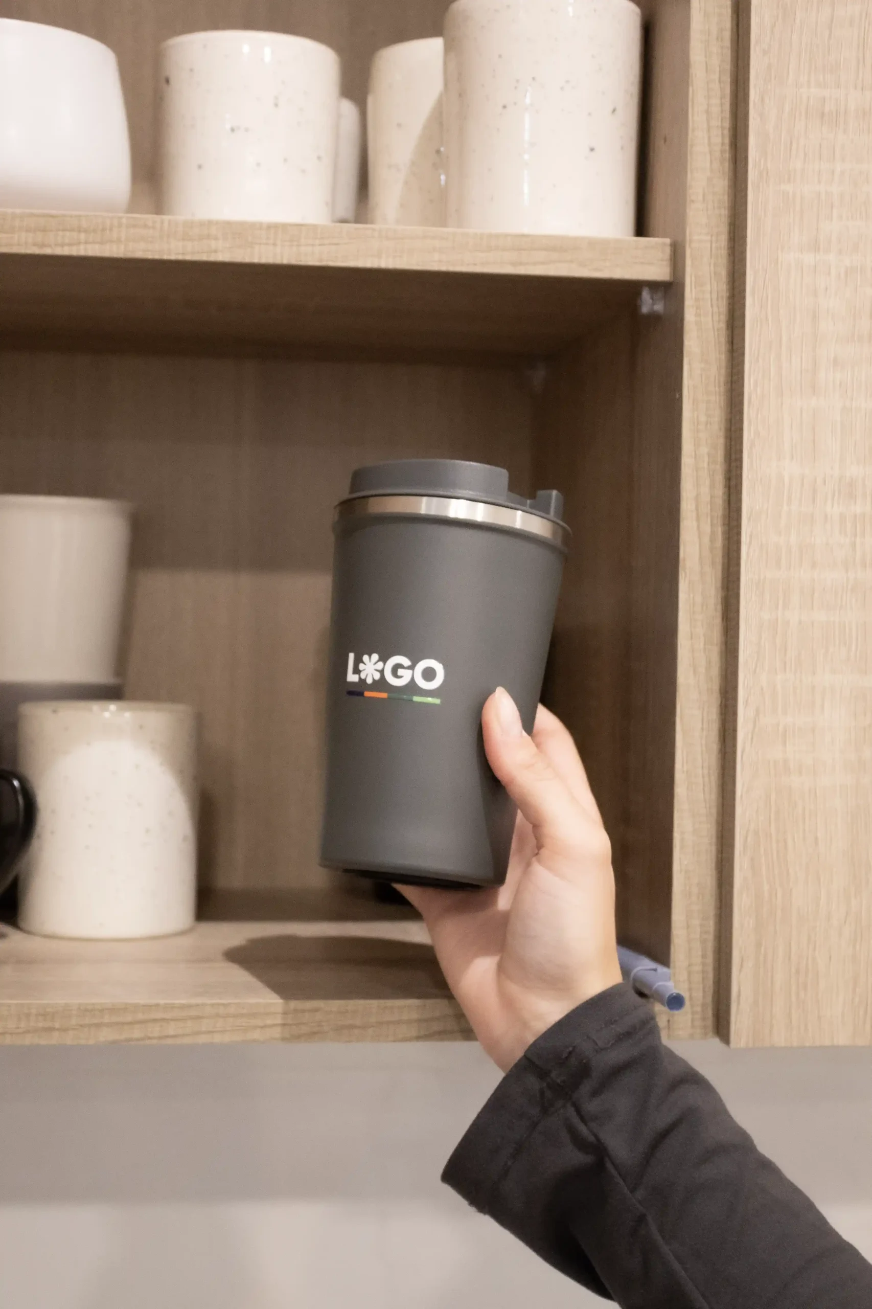 Mano sacando de un armario una taza térmica gris personalizada con logo blanco