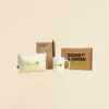 Neceser beige, taza blanca, cuaderno kraft, bolígrafo marrón y caja de cartón personalizados con logo verde