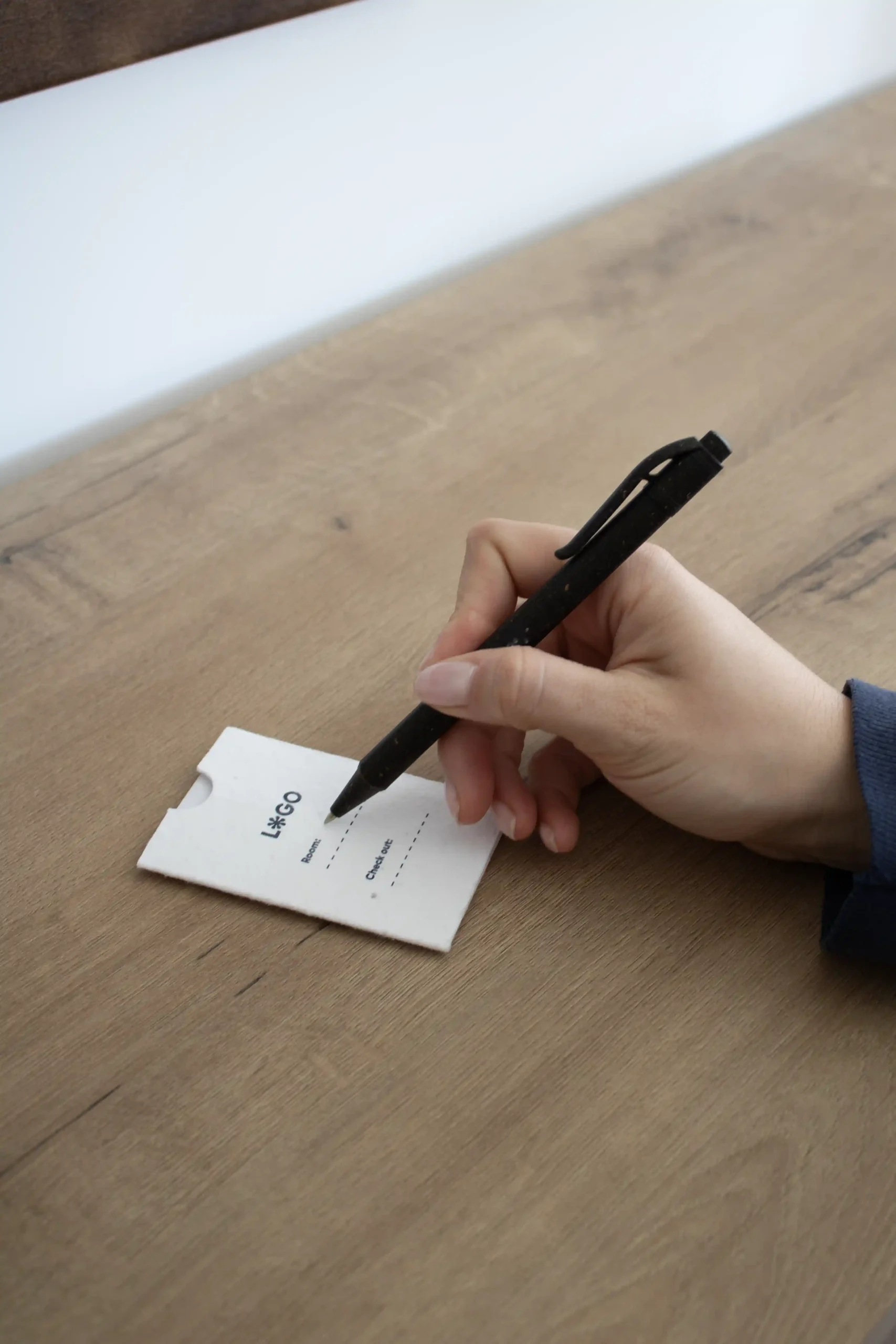 mano escribiendo en una mesa de madera con un bolígrafo en un porta llaves de hotel blanco personalizado con la palabra logo en azul