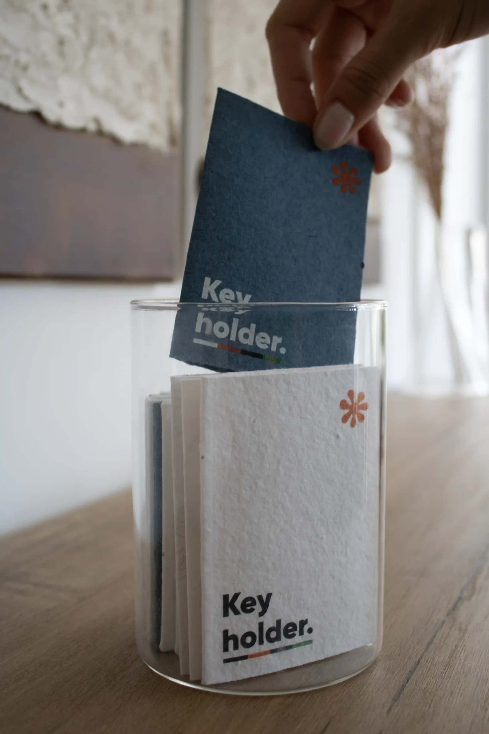 Mano metiendo un porta llaves de hotel personalizado en un jarrón de cristal transparente