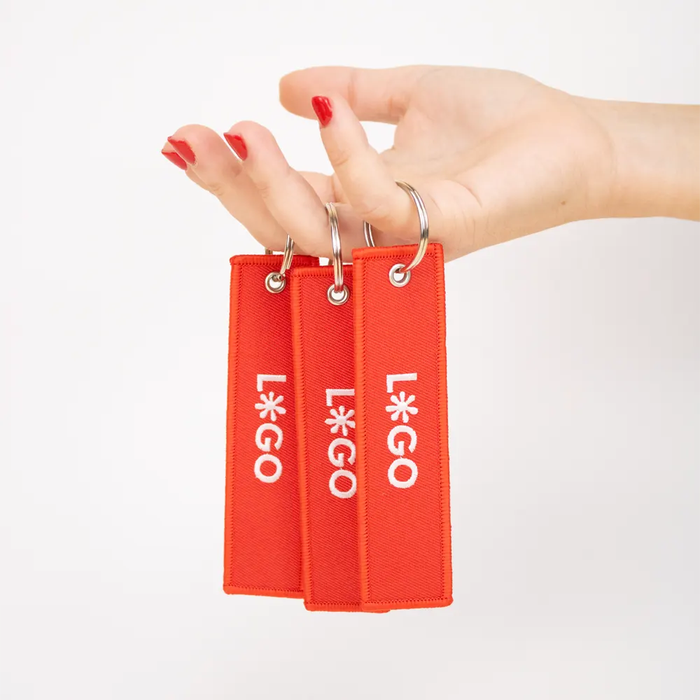 Mano sujetando 3 llaveros de tela rojos personalizados con logo blanco