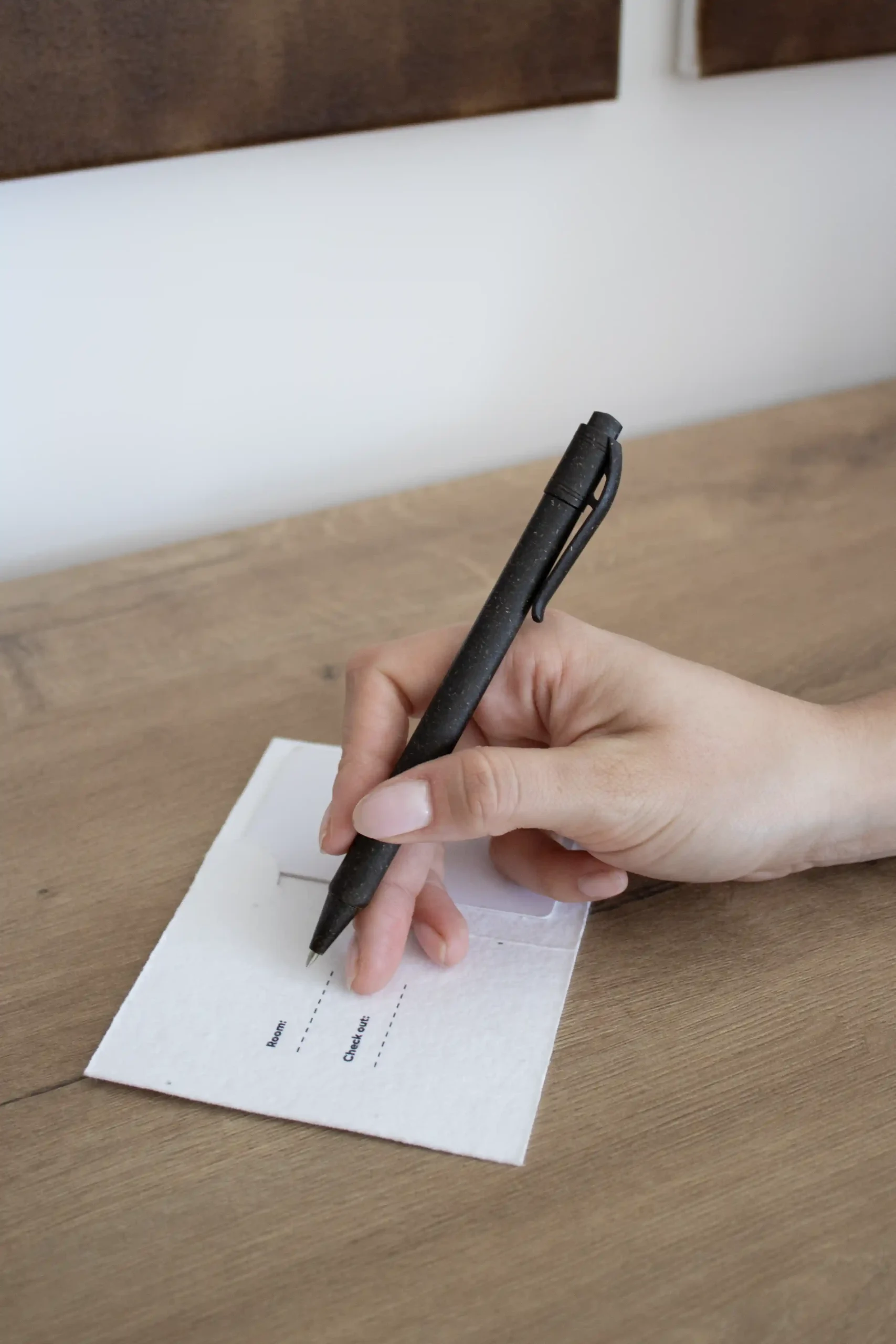 mano escribiendo en una mesa de madera con un bolígrafo en un porta llaves de hotel blanco personalizado con la palabra logo en azul