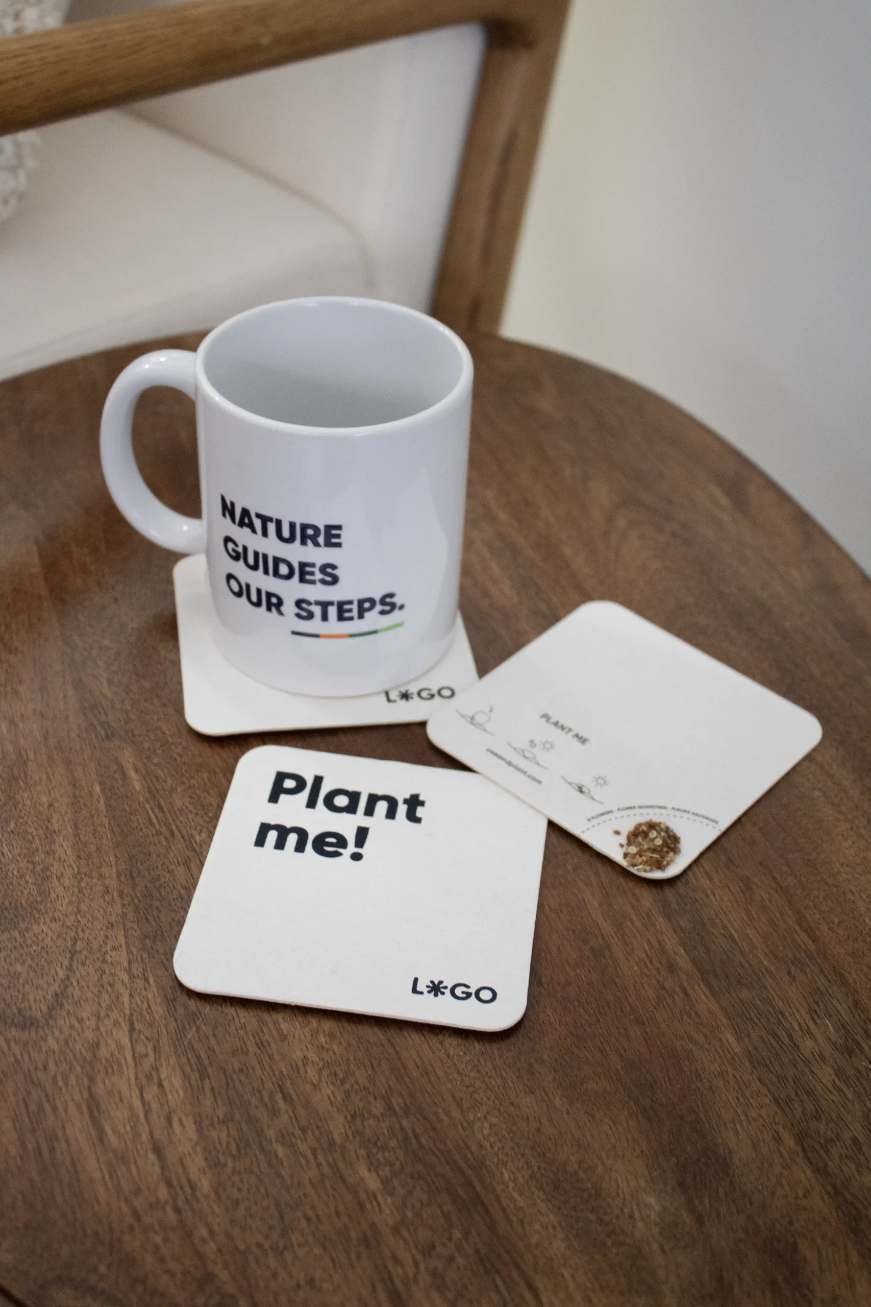 3 posavasos de cartón personalizados junto a una taza blanca sobre una mesa de madera