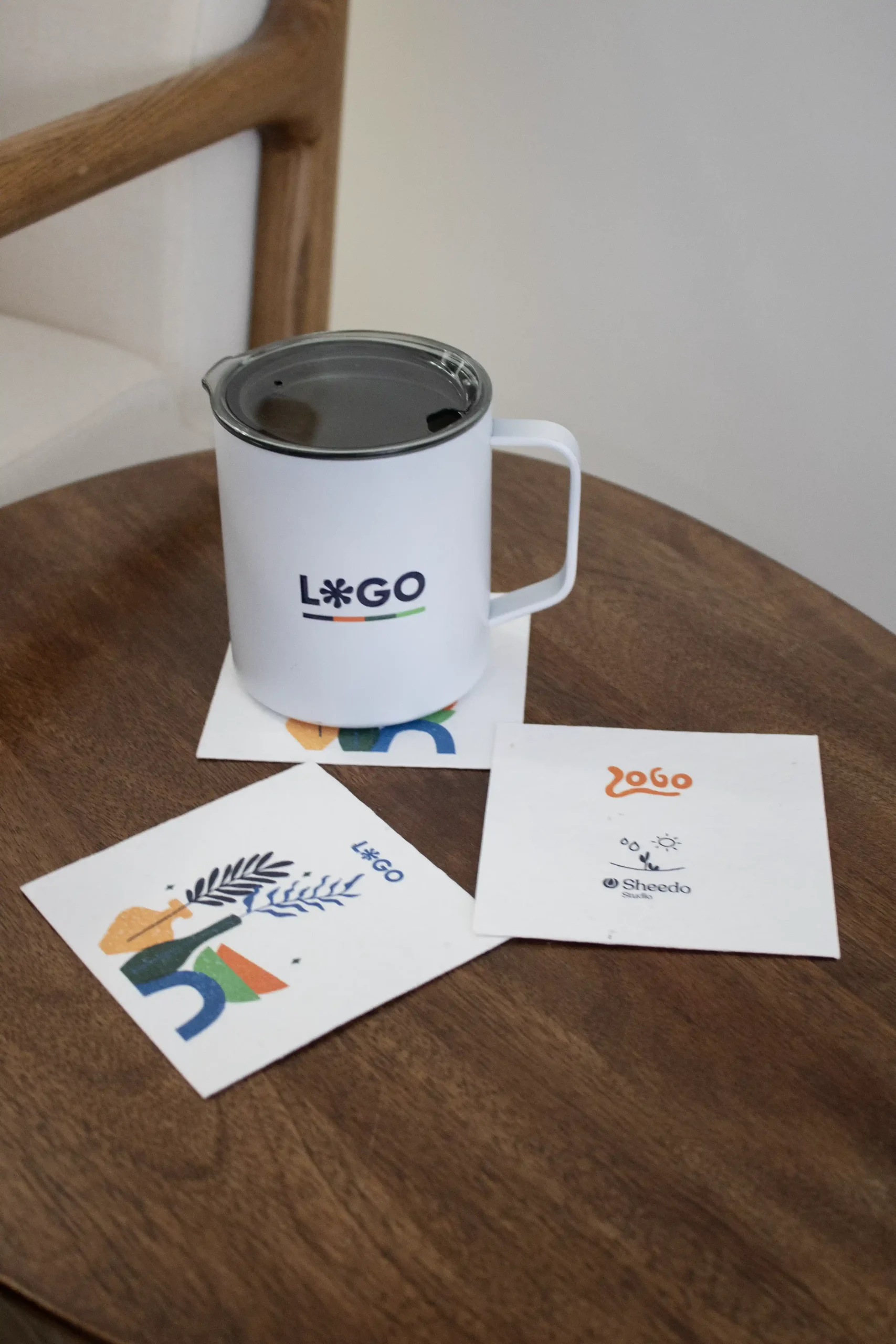 3 posavasos de papel personalizados junto a una taza blanca sobre una mesa de madera