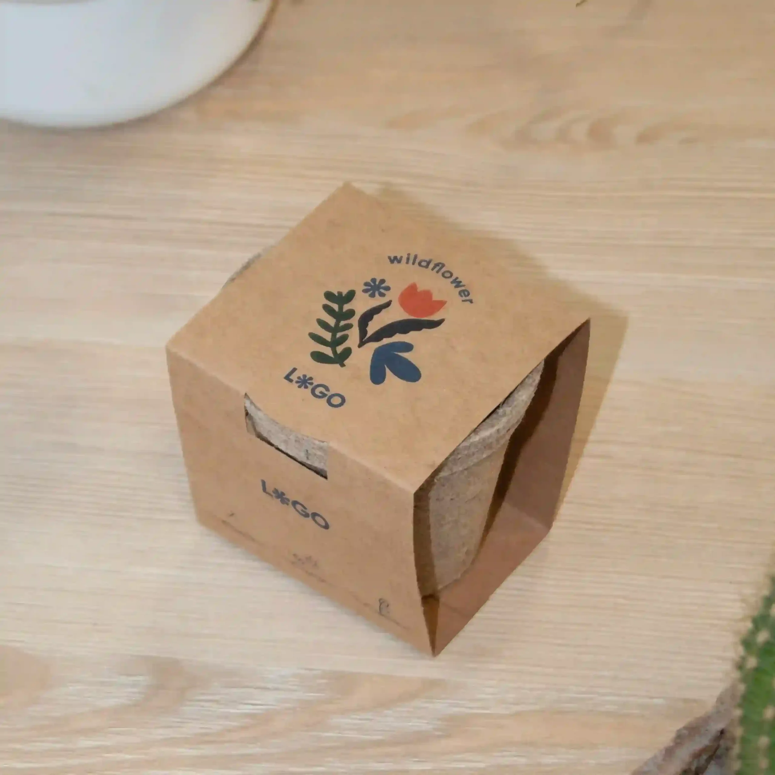 Kit plantable de fibra de coco dentro de un packaging en cartón kraft personalizado sobre una mesa de madera