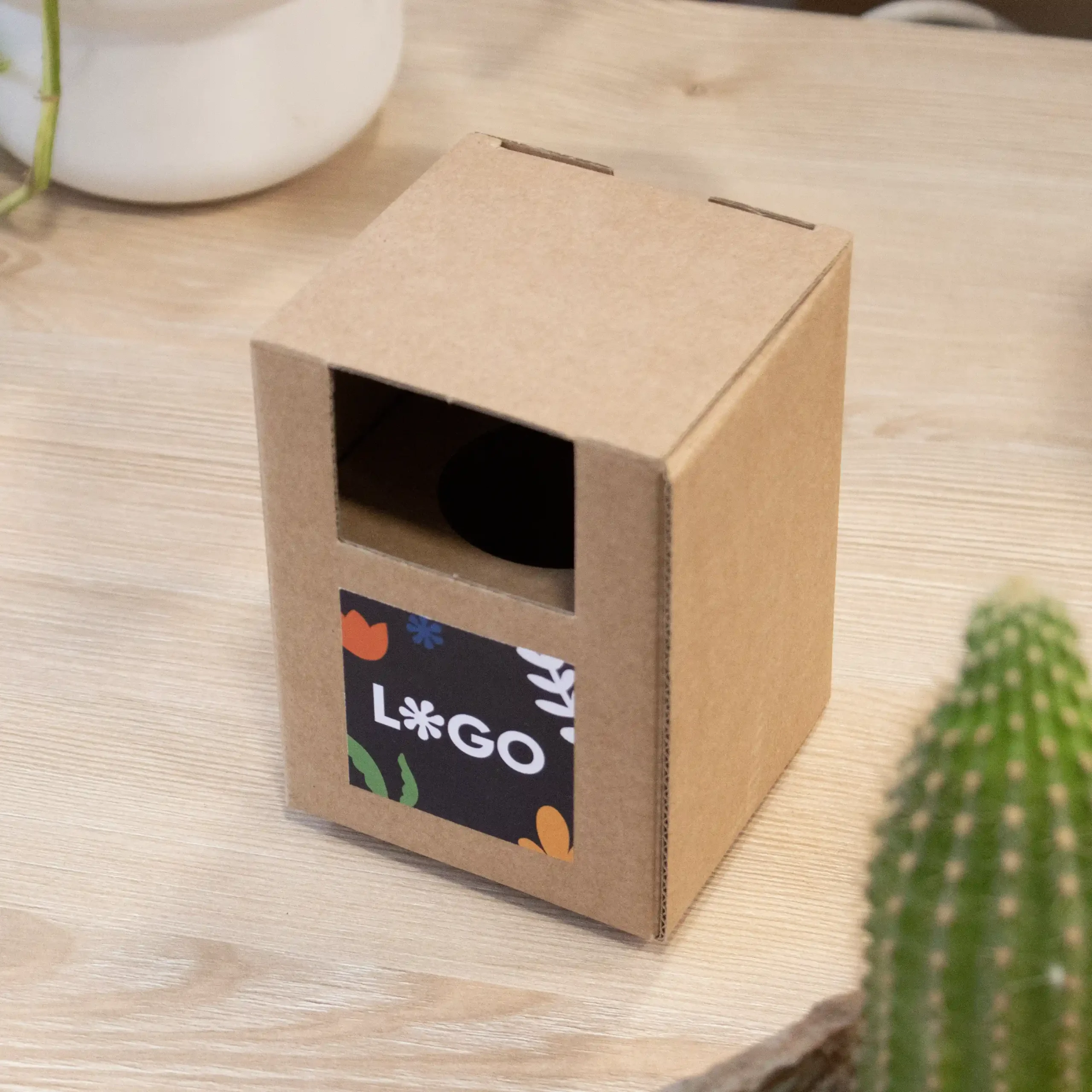 Kit plantable de barro dentro de un packaging en cartón kraft personalizado con una pegatina sobre una mesa de madera