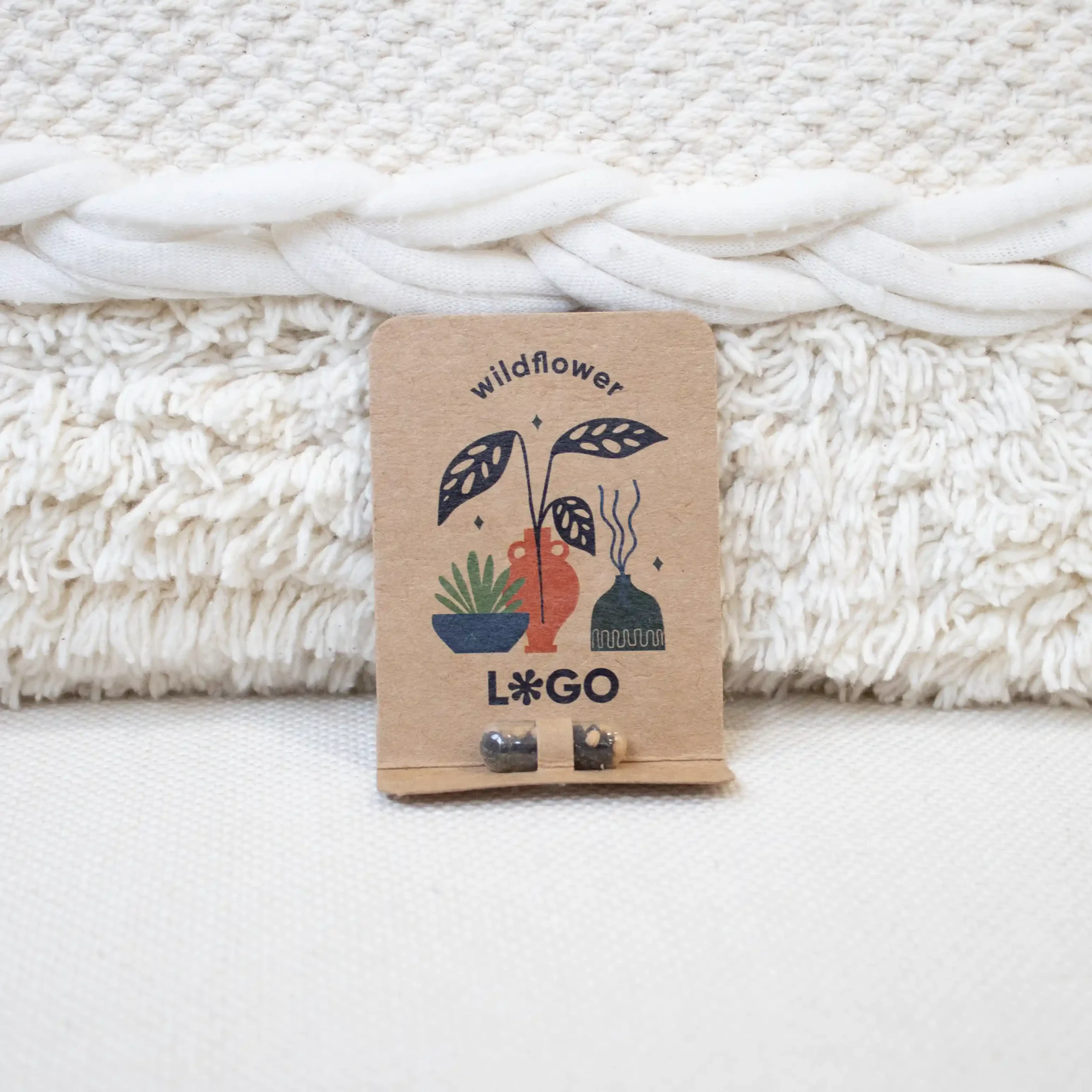Cápsula biodegradable con semillas en su interior con packaging de cartón kraft personalizado apoyada en un cojín blanco