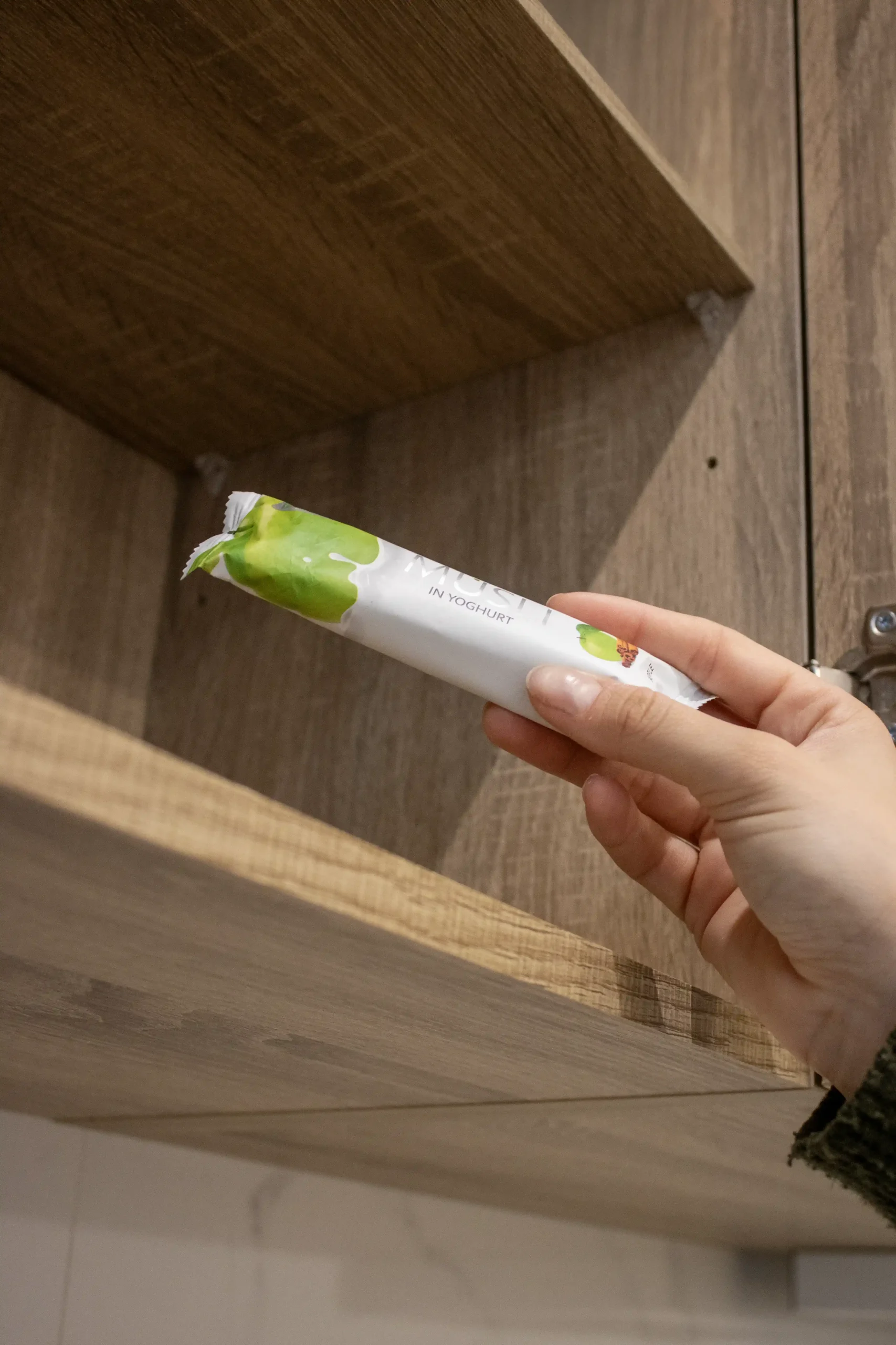 Mano sacando de un armario de madera una barrita de muesli de manzana