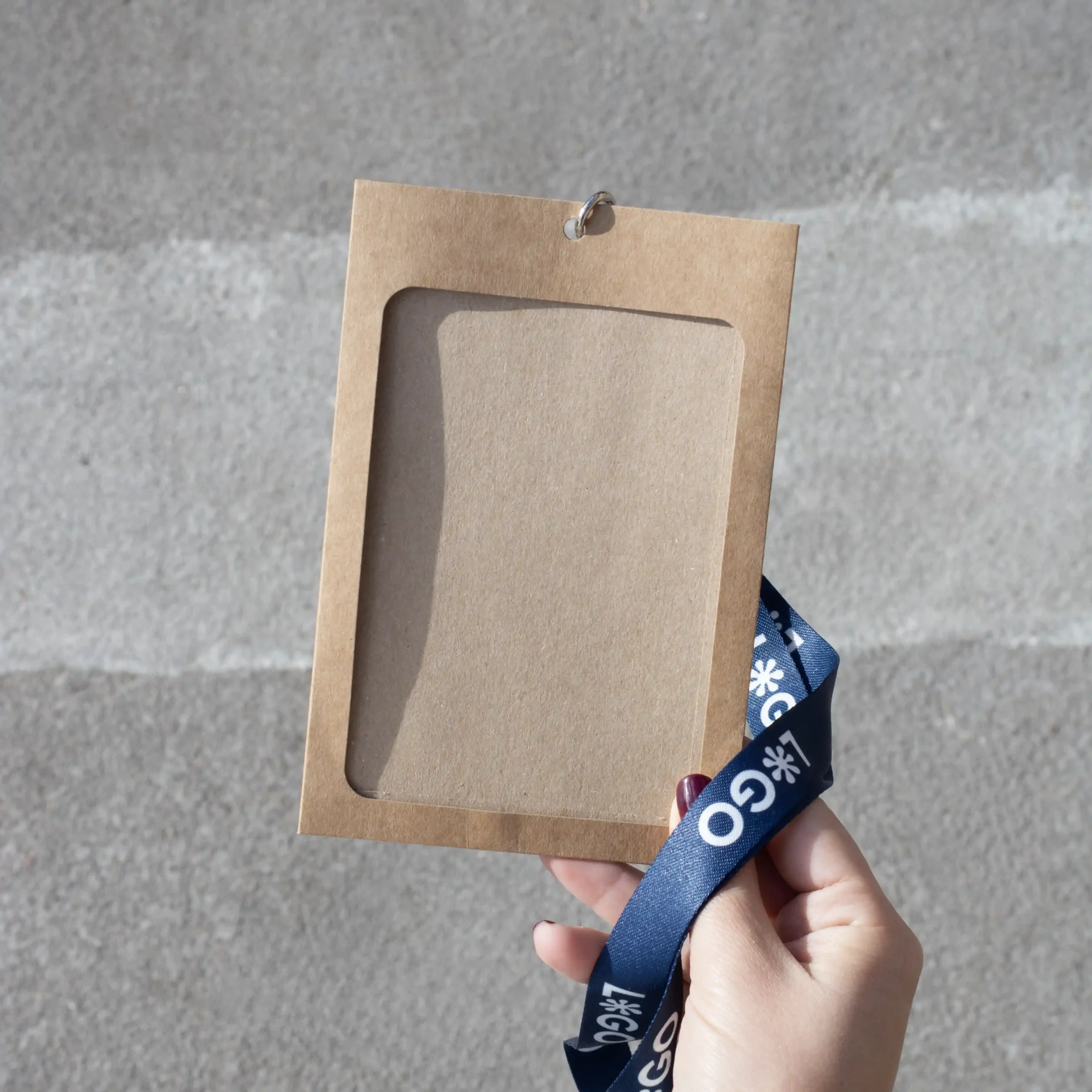 Mano sujetando una funda de acreditación kraft con lanyard de rPET azul personalizado con el texto 'logo' en blanco