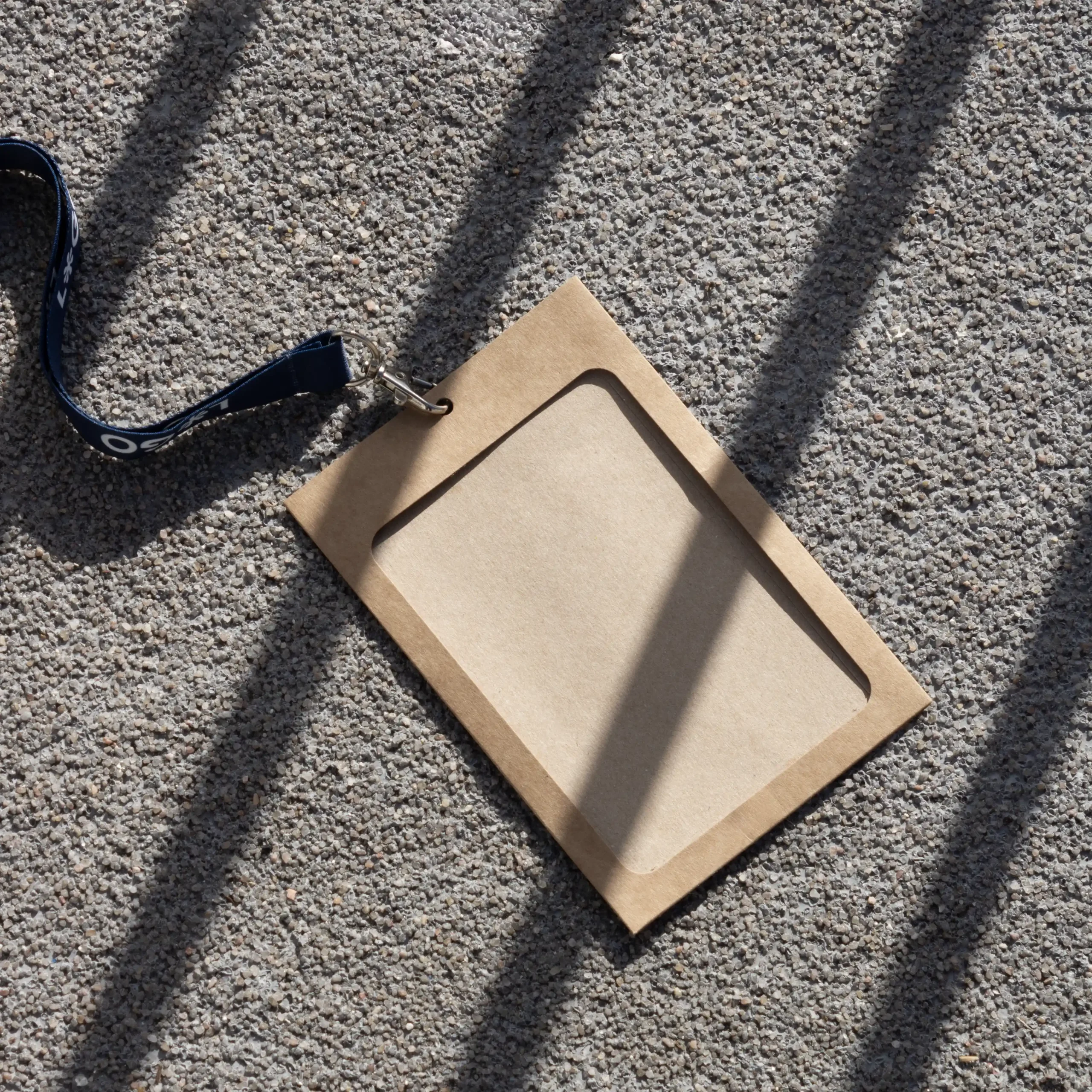 Funda de acreditación kraft con lanyard de rPET azul apoyado en el suelo de la calle
