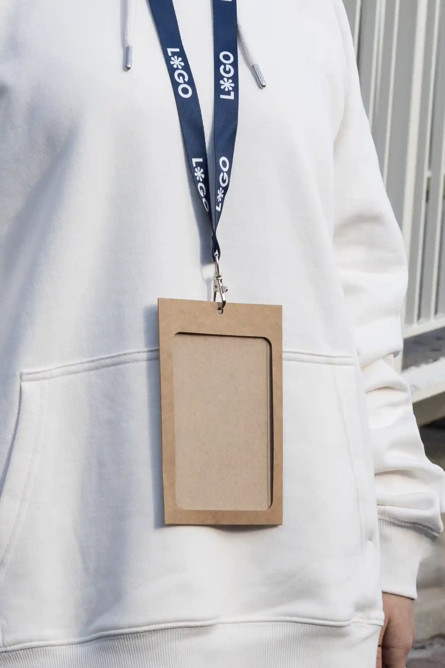 Funda de acreditación kraft y lanyard de rPET azul personalizado colgado del cuello de una persona con jersey blanco