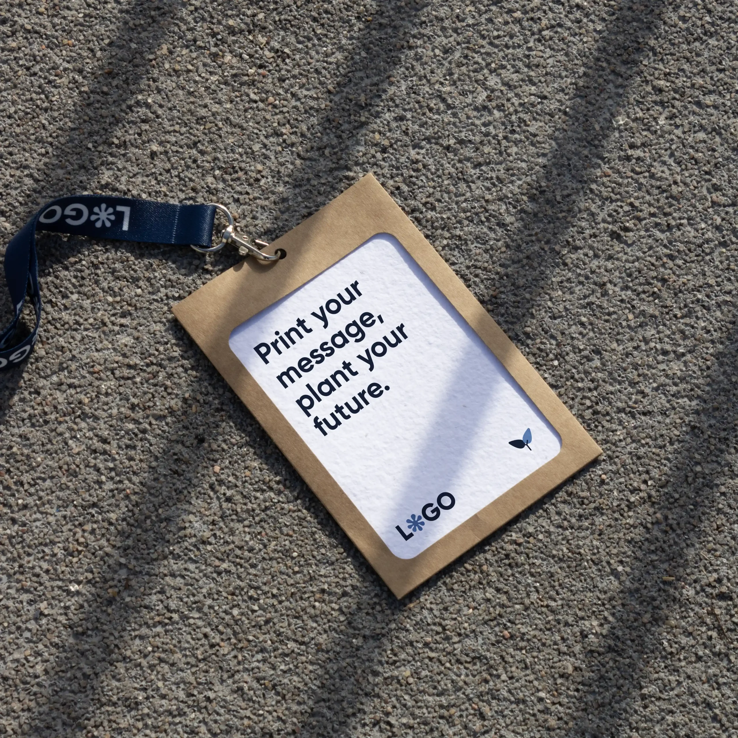 Acreditación personalizada con funda kraft y lanyard de rPET azul personalizado con el texto 'logo' en blanco apoyada en el suelo de la calle
