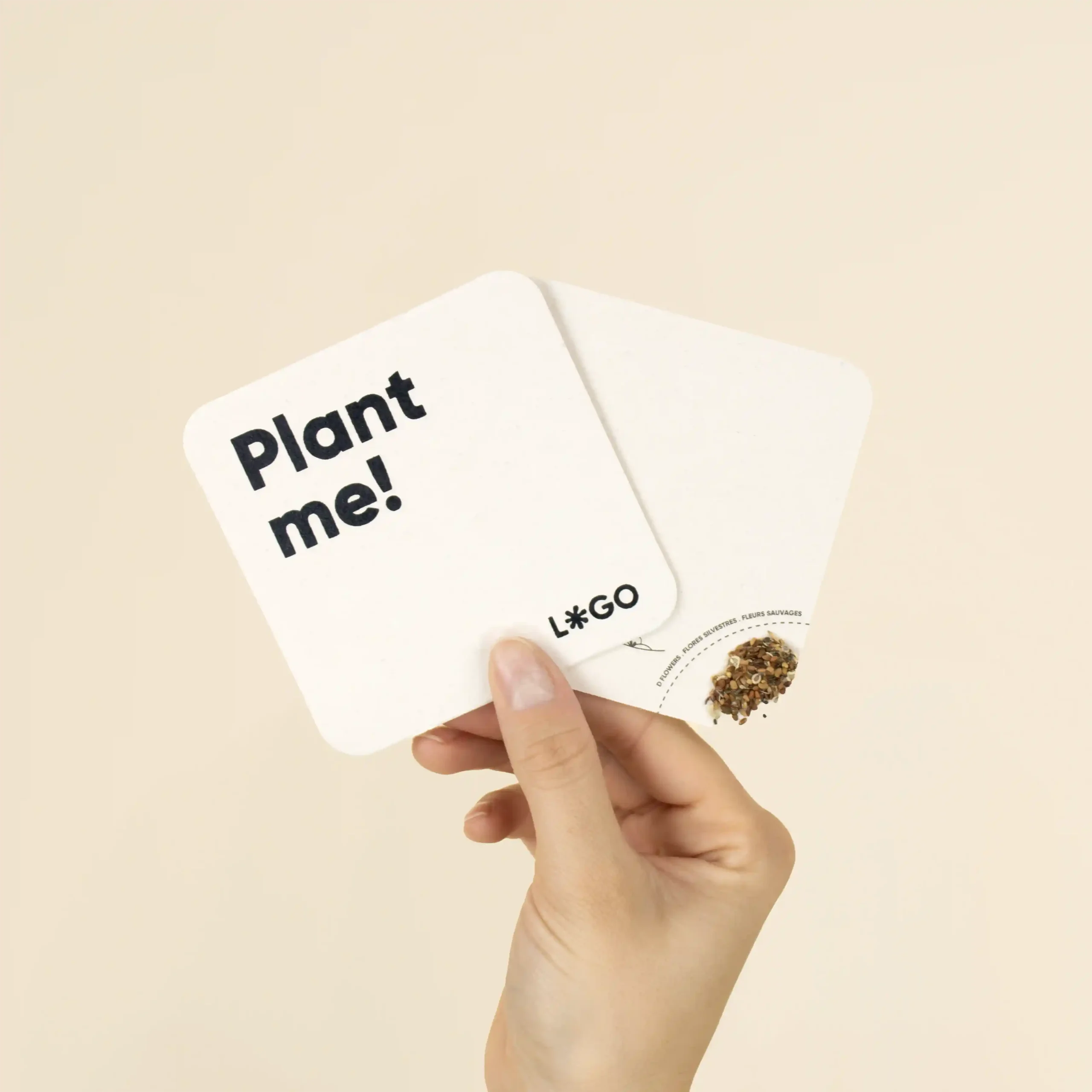 Mano mostrando 2 posavasos de cartón personalizados con semillas pegadas en una esquina