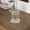 Un posavasos de cartón personalizado de bajo de un vaso lleno de agua sobre una superficie de madera