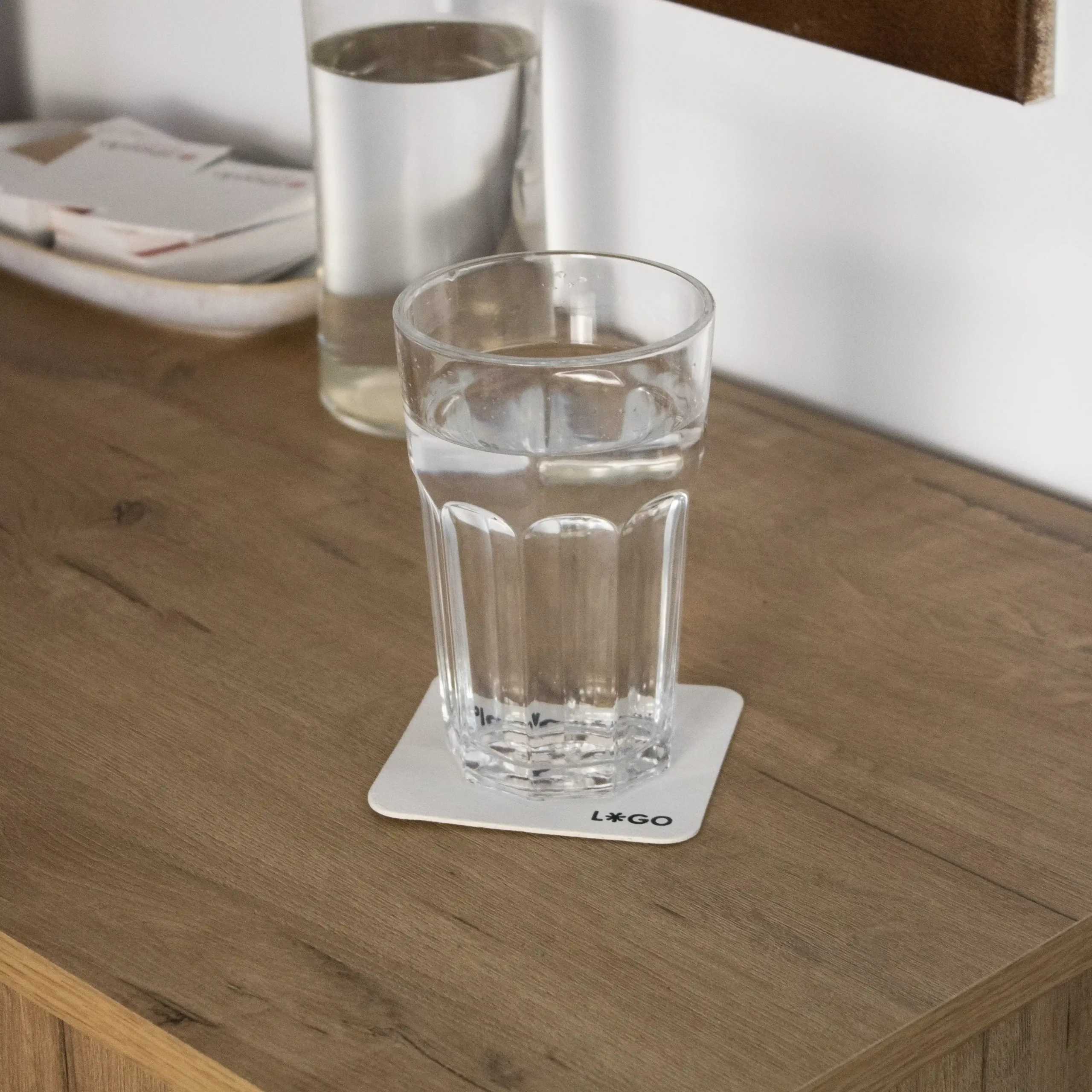 Un posavasos de cartón personalizado de bajo de un vaso lleno de agua sobre una superficie de madera