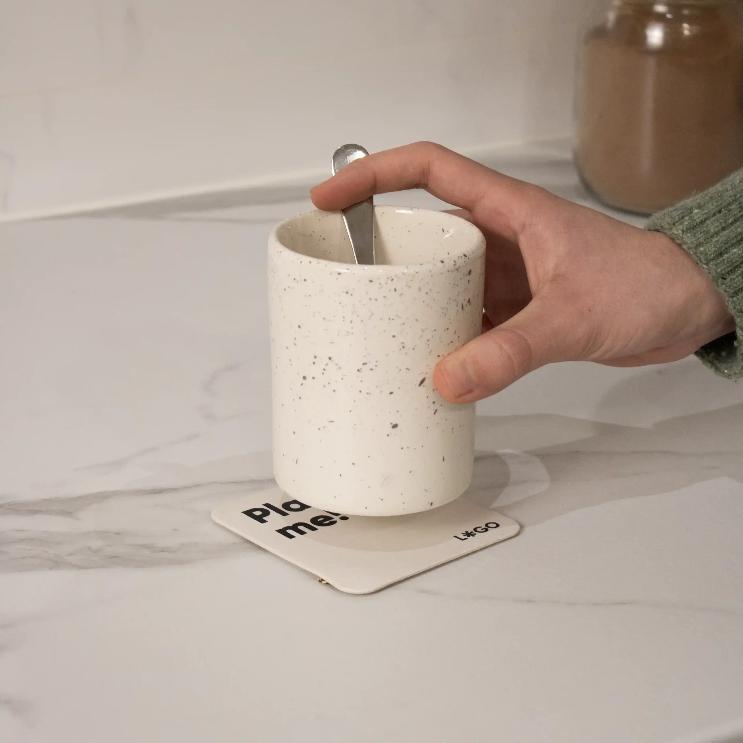 Una mano dejando una taza blanca sobre un posavasos de cartón personalizado