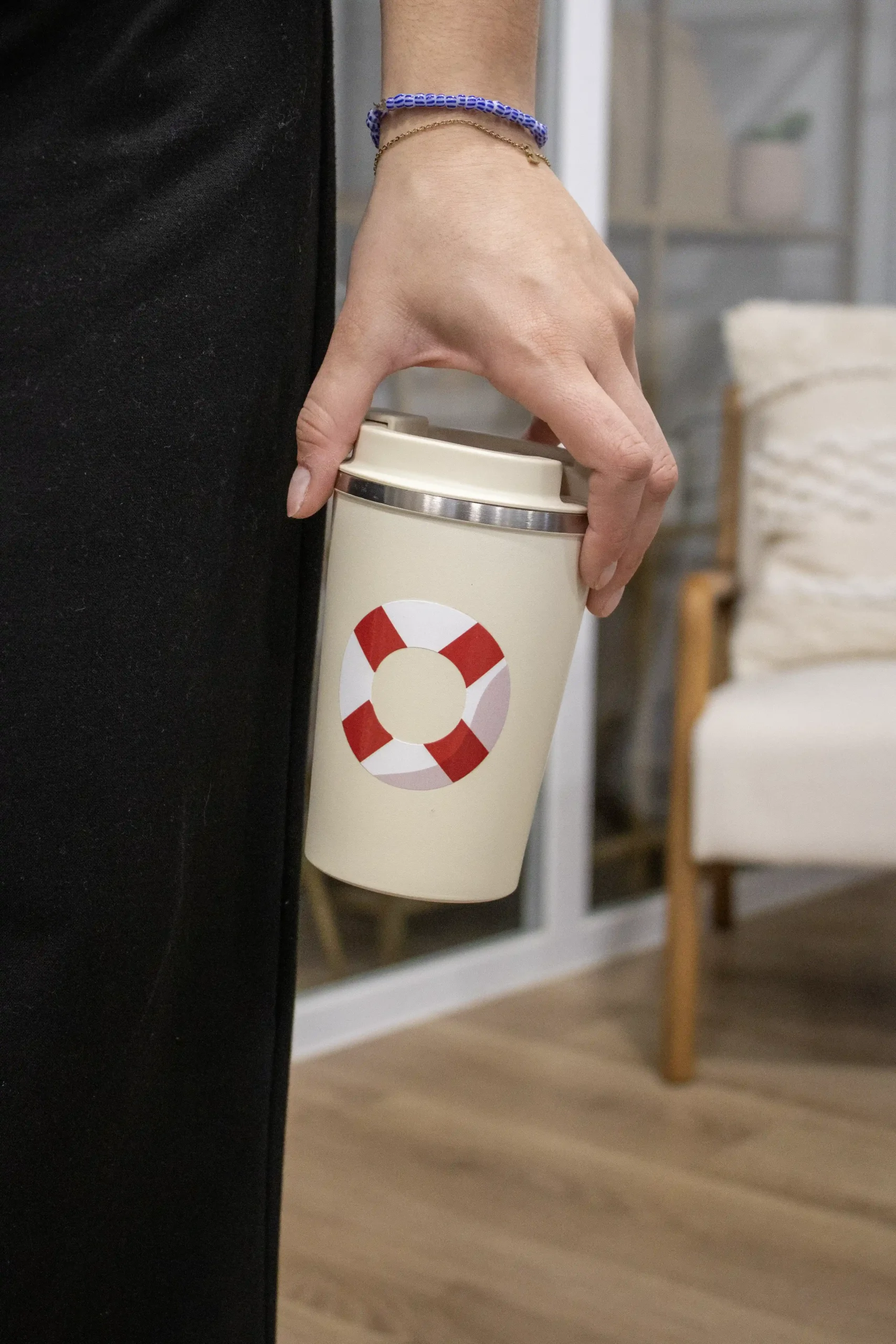 Mano sujetando una taza take away beige personalizada con una ilustración de un flotador rojo y blanco