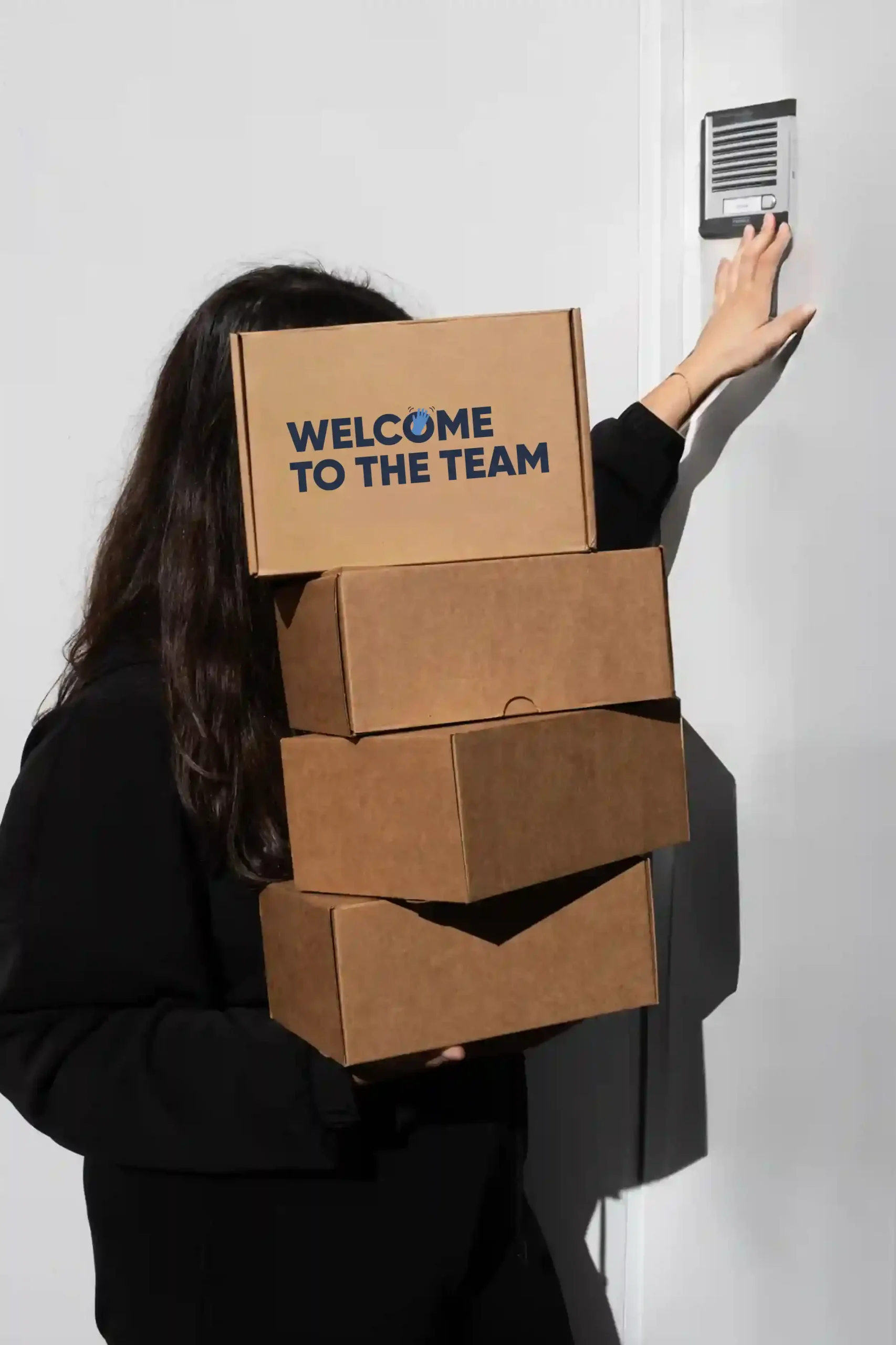 Chica cargando cajas de cartón personalizadas con el texto 'welcome to the team'