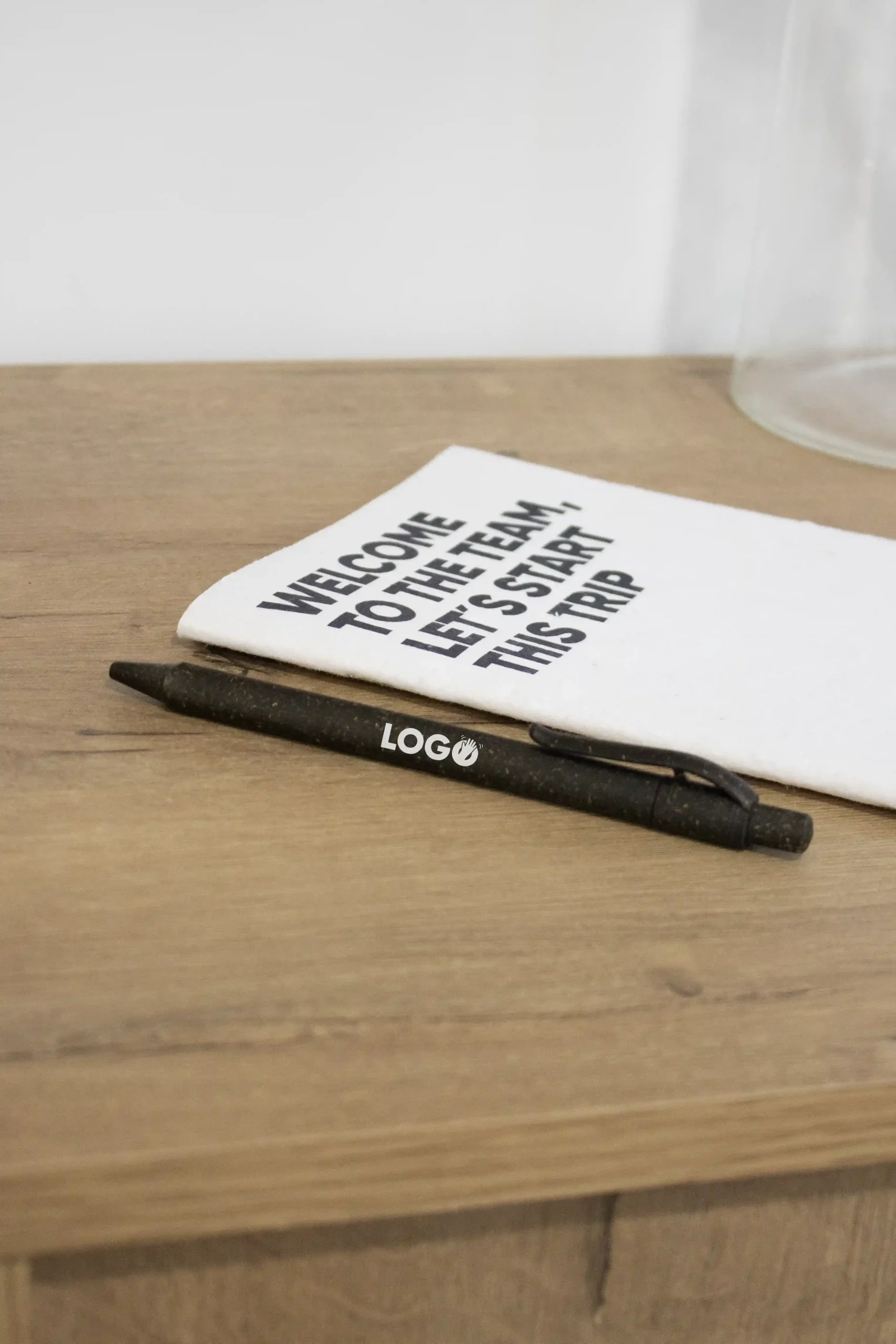Bolígrafo ecológico de hierba personalizado con la palabra logo en blanco junto a un cuaderno plantable blanco personalizado sobre una superficie de madera