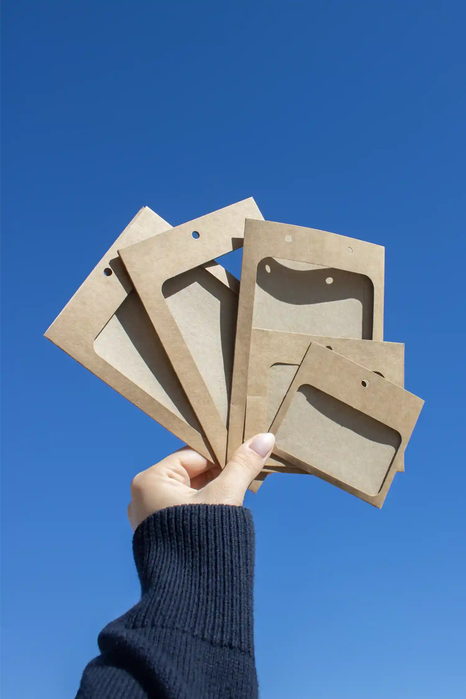 Mano mostrando un conjunto de fundas de acreditación en cartón kraft marrón con el cielo de fondo