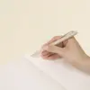 Mano sujetando un bolígrafo beige escribiendo sobre las páginas interiores de un cuaderno