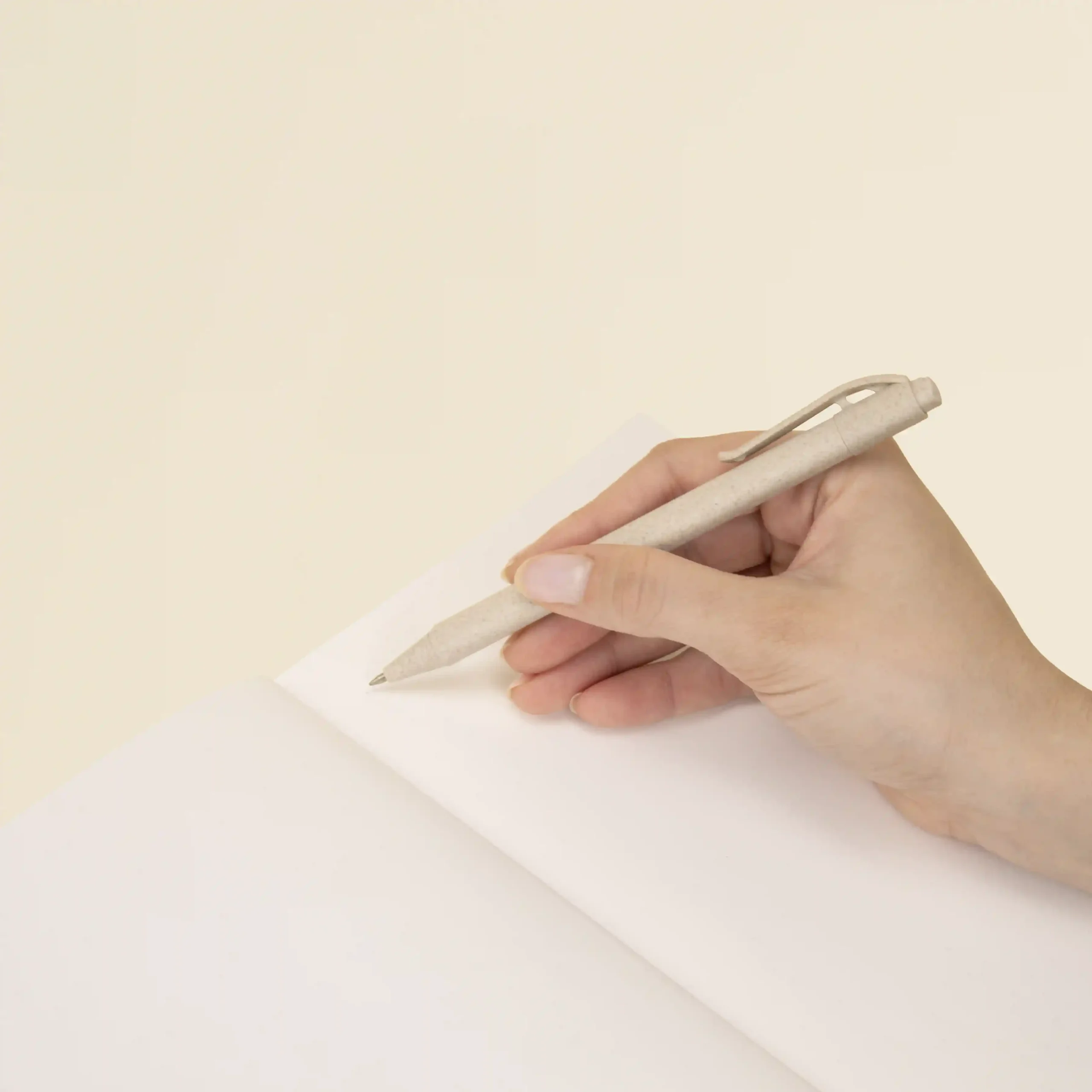Mano sujetando un bolígrafo beige escribiendo sobre las páginas interiores de un cuaderno