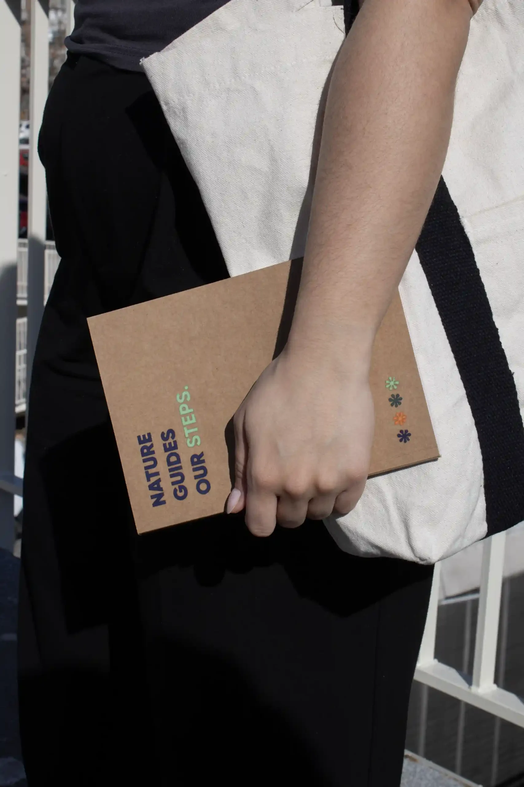 Chica llevando en la mano un cuaderno ecológico kraft personalizado con el texto 'Nature guides our steps'