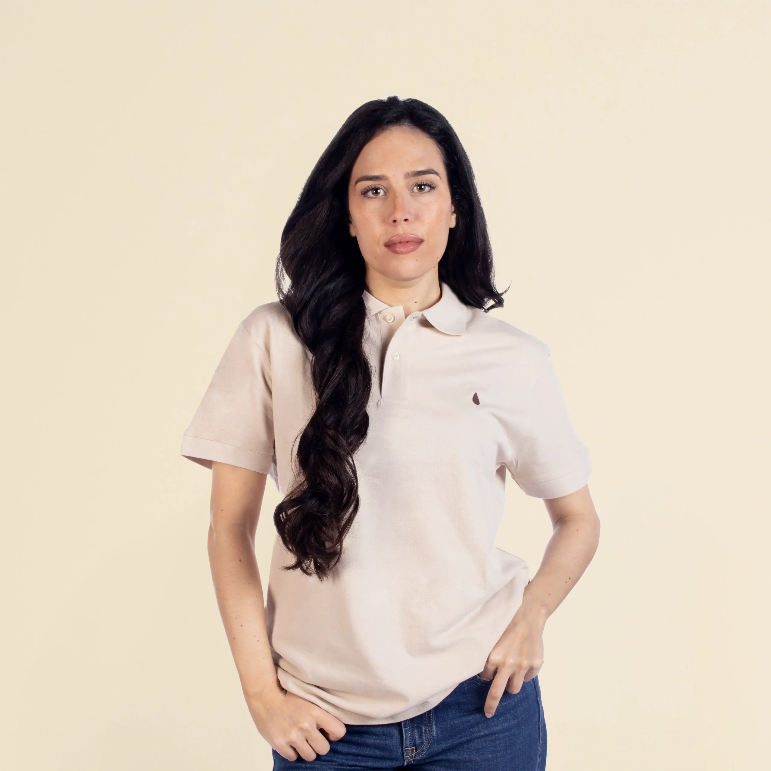 Chica de frente llevando un polo beige personalizado con una ilustración de una gota de agua marrón pequeña