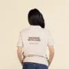 Chica de espaldas llevando con un polo beige personalizado con el texto en marrón "Wearing with care"