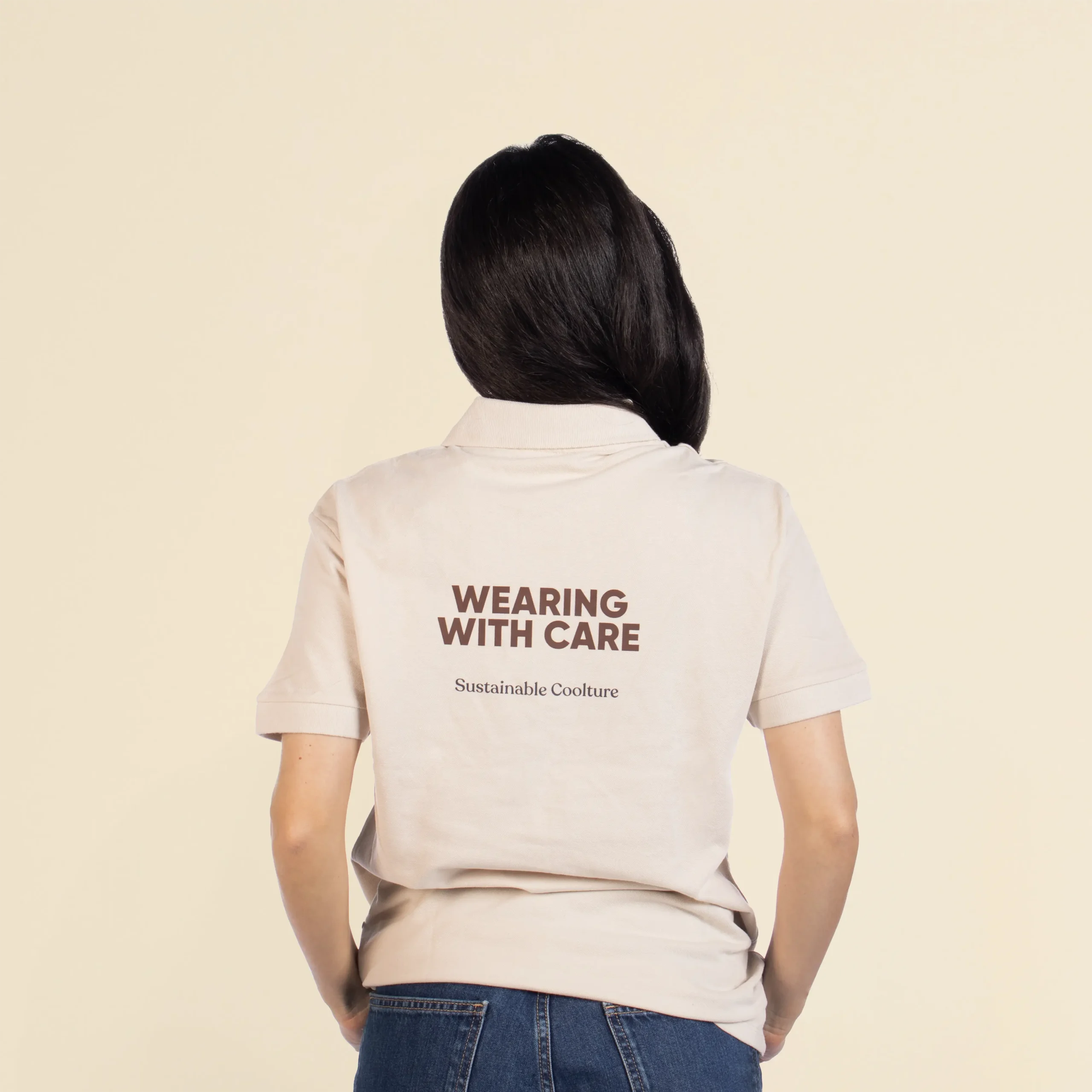 Chica de espaldas llevando con un polo beige personalizado con el texto en marrón "Wearing with care"