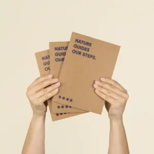 Dos manos sujetando 3 cuadernos plantables kraft personalizados con el texto 'Nature guides our steps'