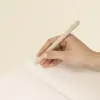 Mano sujetando un bolígrafo beige escribiendo sobre las páginas interiores de un cuaderno