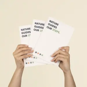 Dos manos sujetando 3 cuadernos plantables blancos personalizados con el texto 'Nature guides our steps'