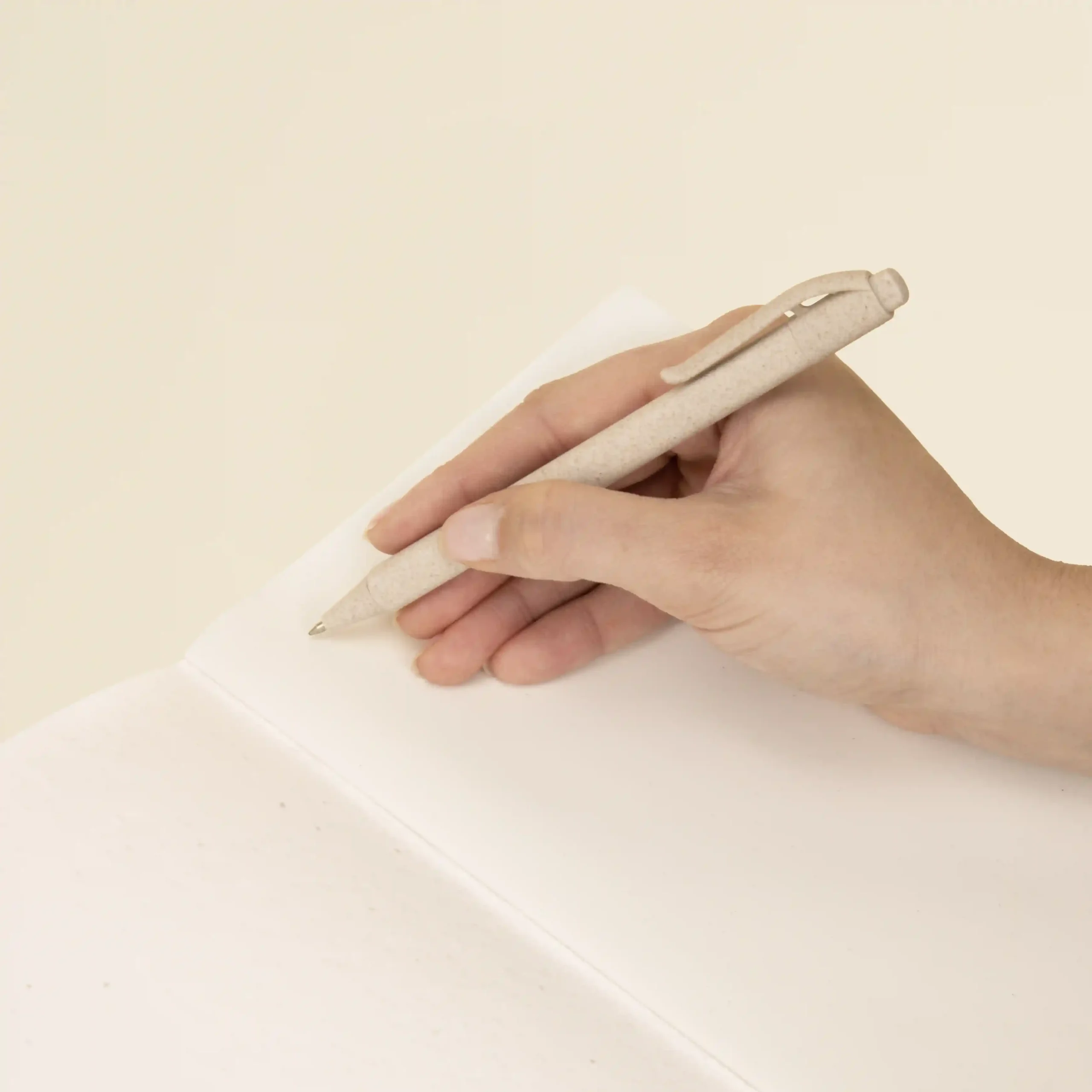 Mano sujetando un bolígrafo beige escribiendo sobre las páginas interiores de un cuaderno