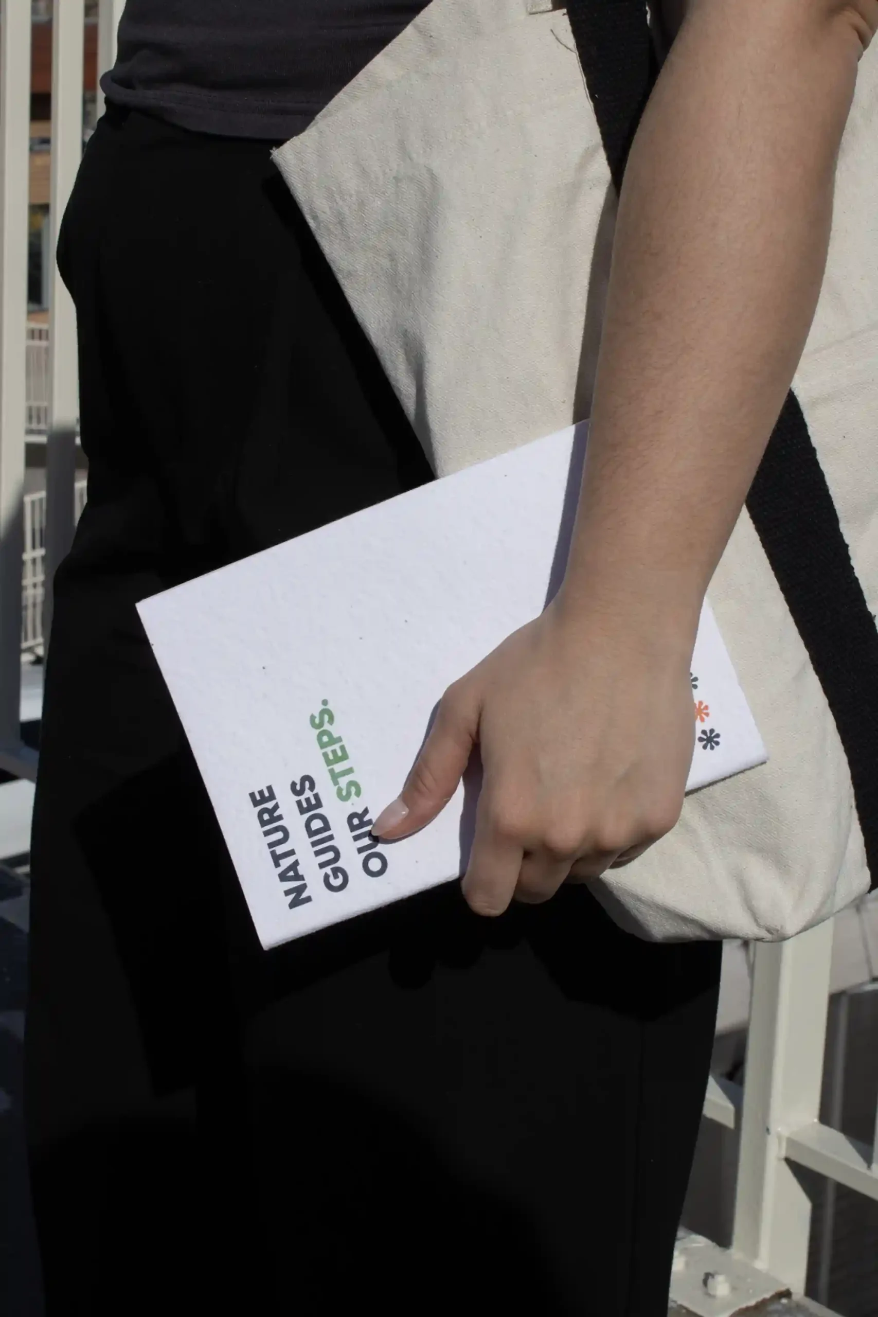 Chica llevando en la mano un cuaderno plantable blanco personalizado con el texto 'Nature guides our steps'