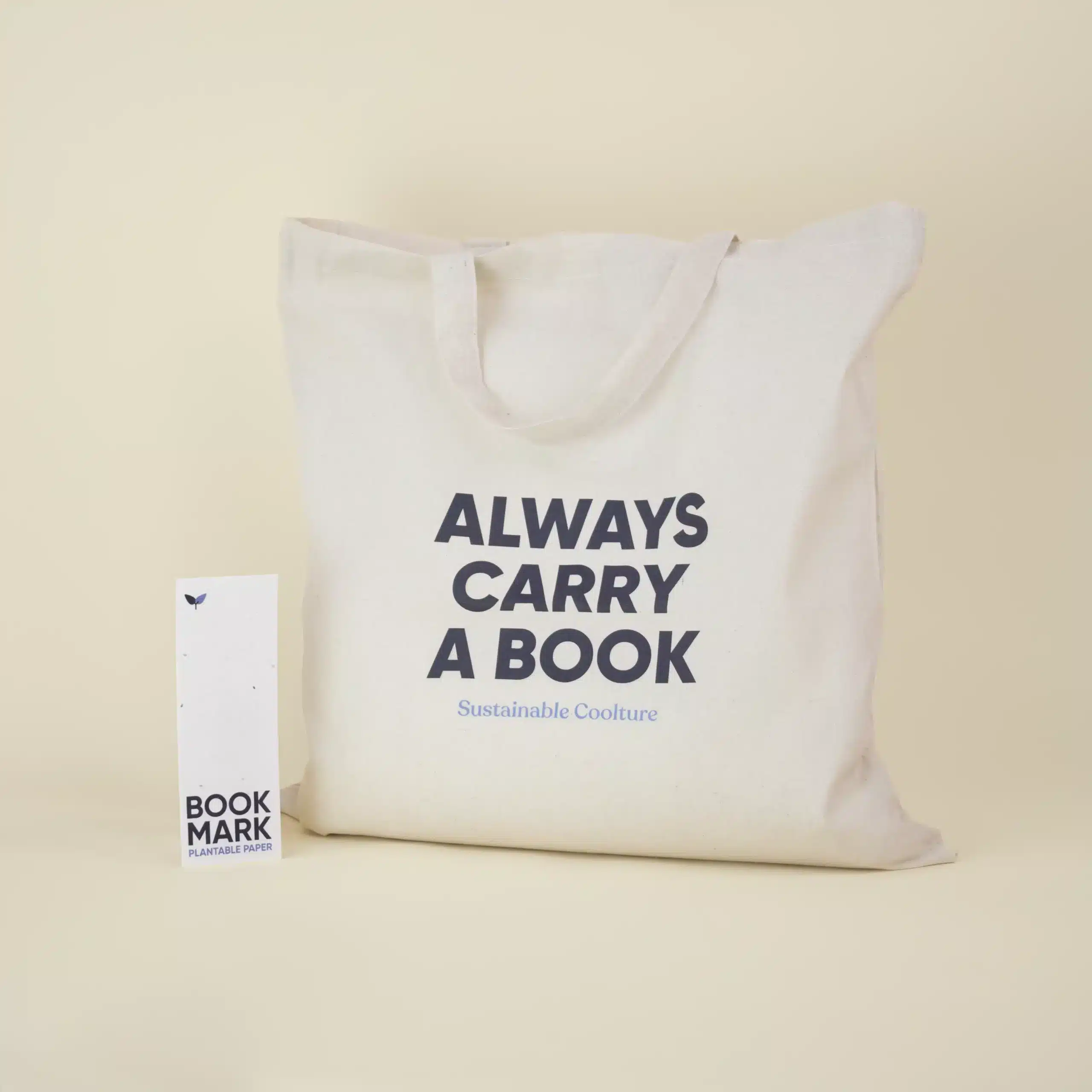 Bolsa de algodón beige personalizada con el texto 'Always carry a book' junto a un marcapáginas de papel plantable personalizado