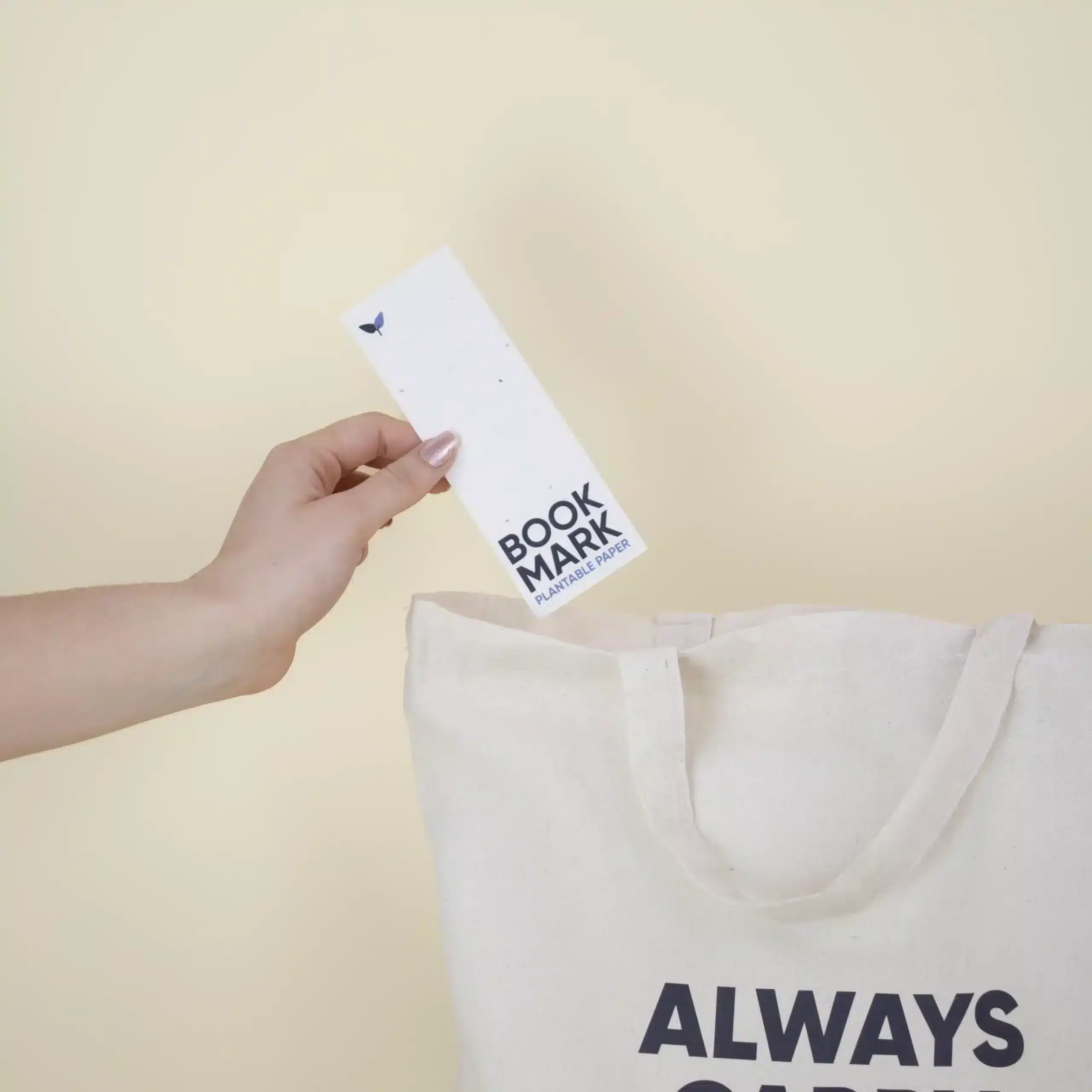 Mano metiendo un marcapáginas de papel plantable personalizado en una bolsa de algodón beige
