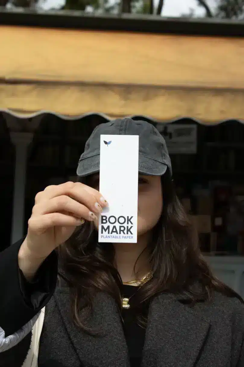 Chico llevando una bolsa de algodón beige personalizada con el texto 'Always carry a book' y sujetando un móvil y un marcapáginas personalizado con su mano