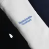 Detalle del texto 'sustainable coolture' bordado en una sudadera con capucha blanca