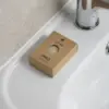 Jabón artesanal dentro una caja marrón kraft personalizada colocada sobre el mueble de un lavabo