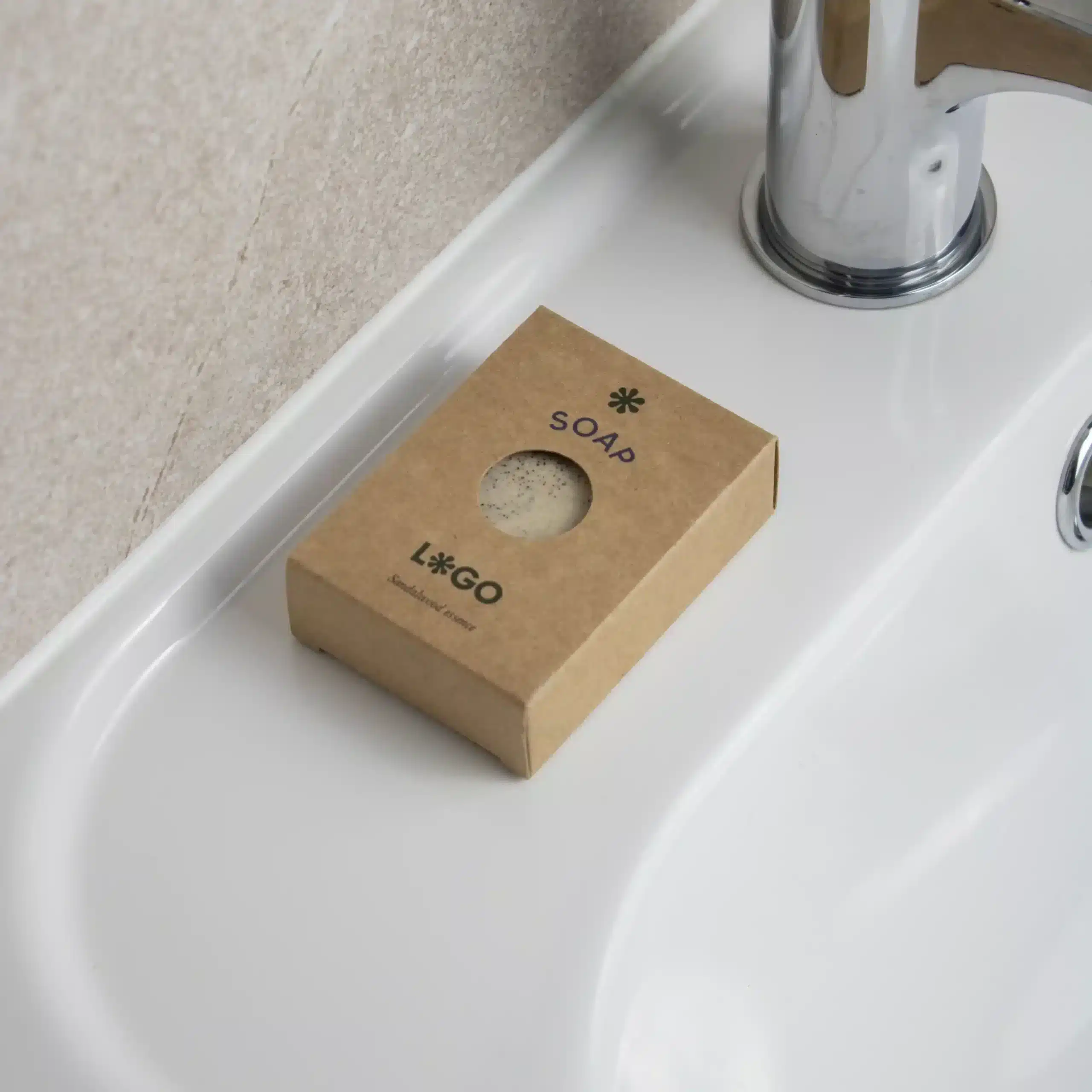 Jabón artesanal dentro una caja marrón kraft personalizada colocada sobre el mueble de un lavabo