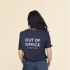 Chica morena de espaldas llevando jeans y una camiseta azul personalizada con el texto 'out of office'