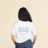 Chica morena de espaldas llevando jeans y una camiseta blanca personalizada con el texto 'out of office'